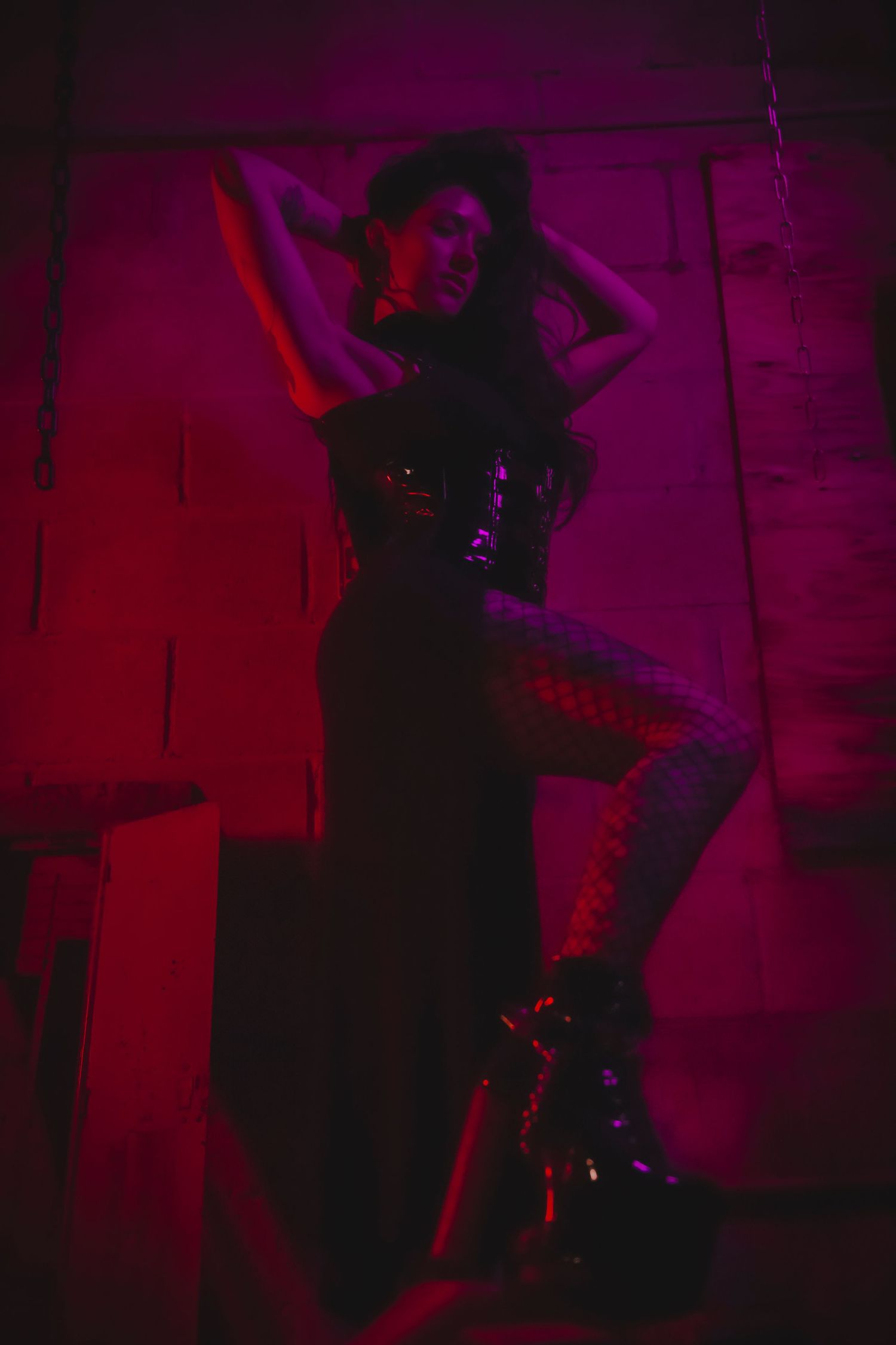 A silhouetted figure performs on stage against a deep red and purple backlit backdrop during a dimly lit performance.