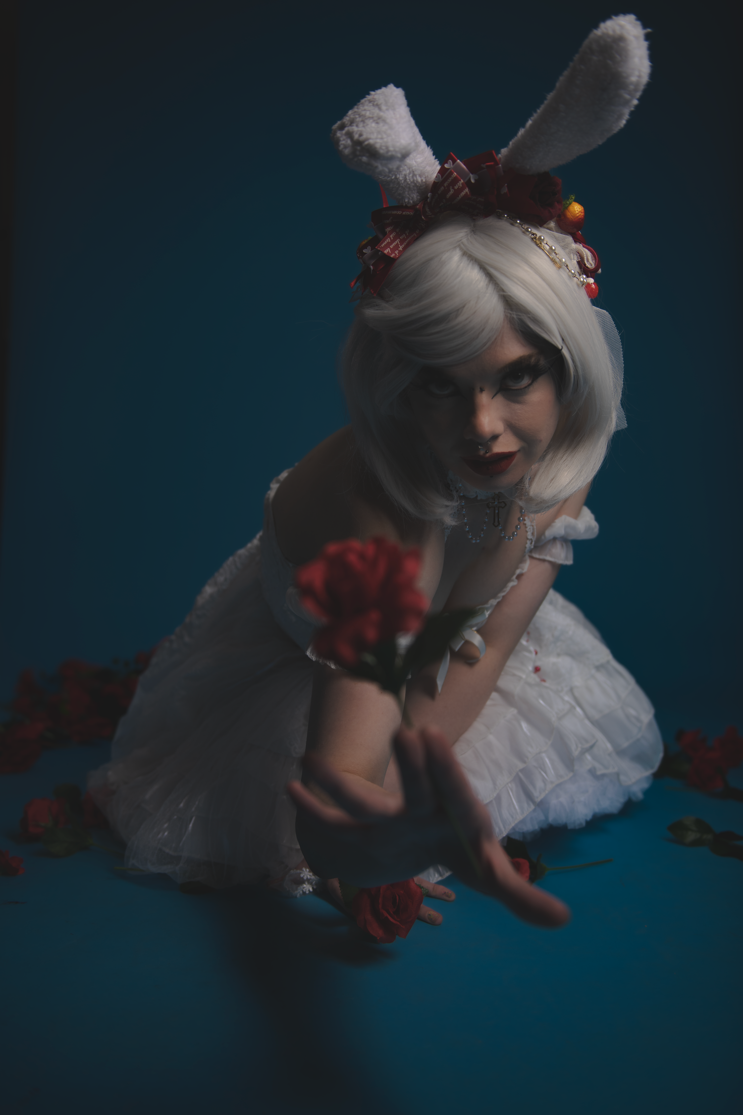 A person in a white dress and rabbit ears poses dramatically against a dark blue background with scattered autumn leaves.