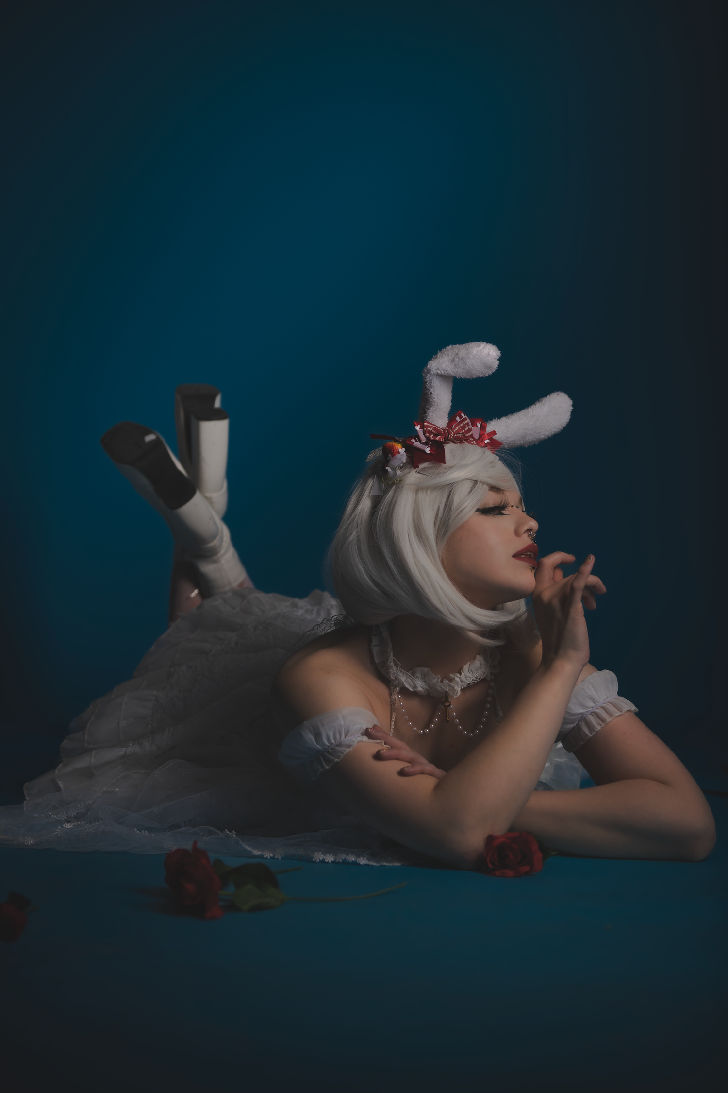 Reclining figure in white costume with scattered red flowers on dark surface.