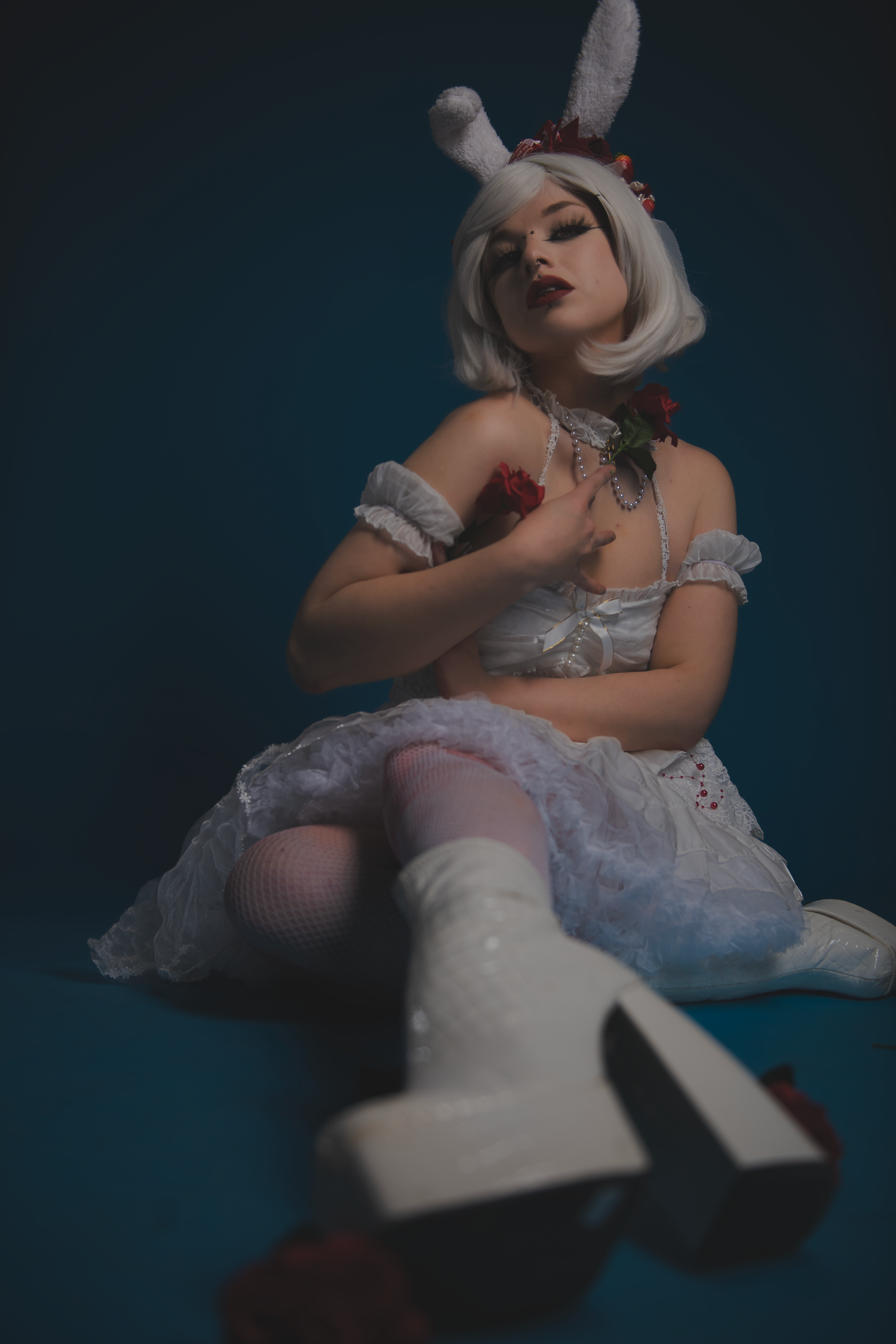 Artistic fashion portraits of a figure in white ruffled dress posing expressively against dark blue background.