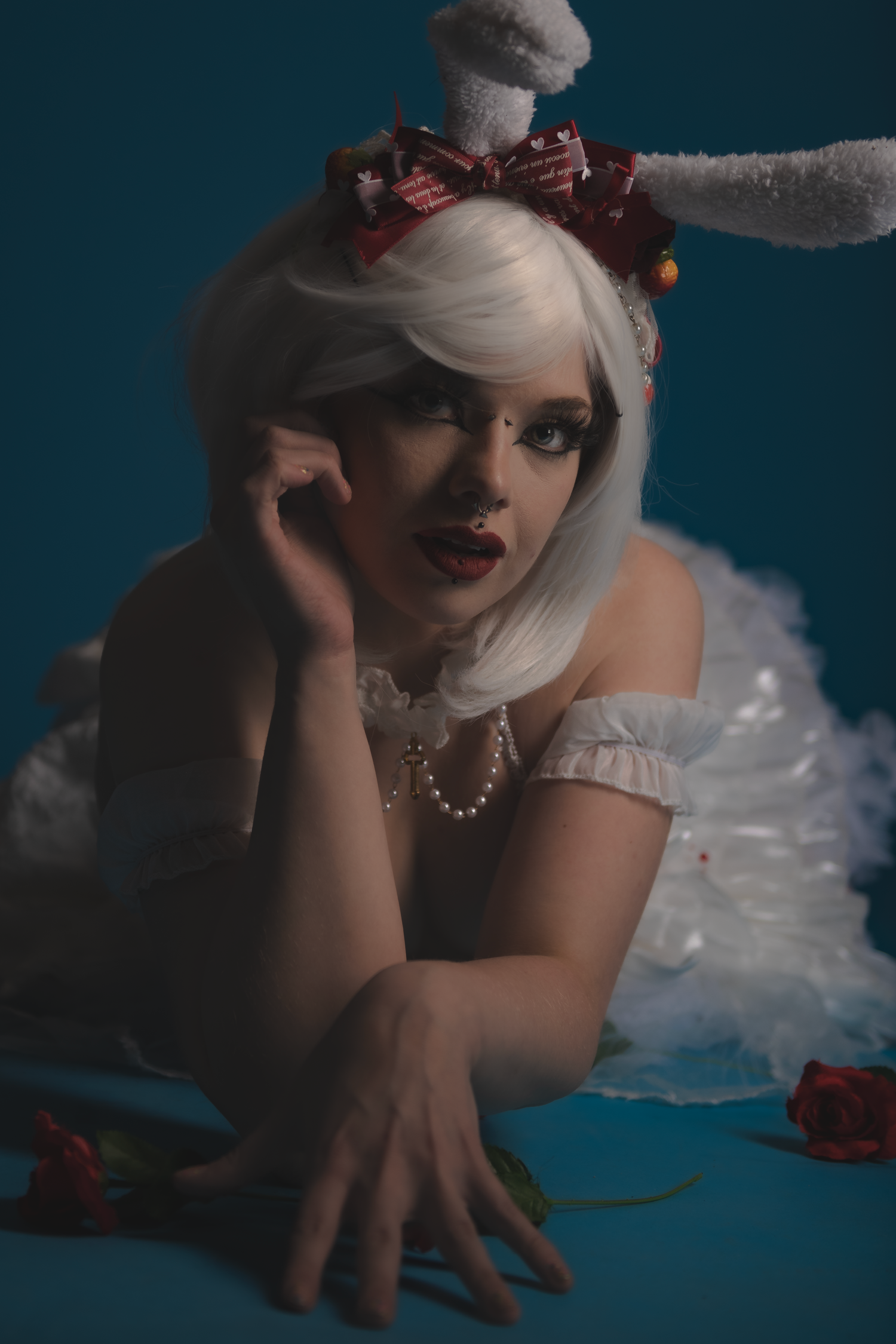 Stylized fashion photo of model in white dress and bunny headpiece against teal background.