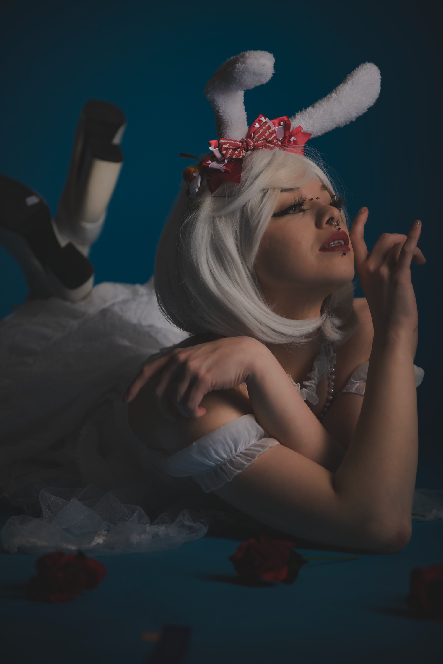 Dramatic low-light portrait of figure in white dress on dark surface.