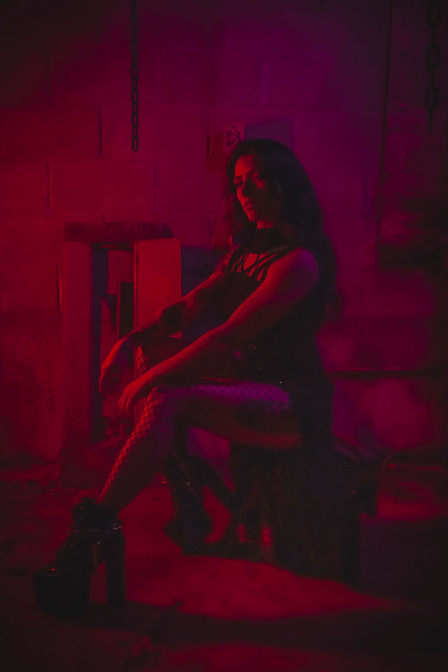 A dramatic scene lit in deep red shows a silhouetted figure seated on what appears to be furniture in a dark room.