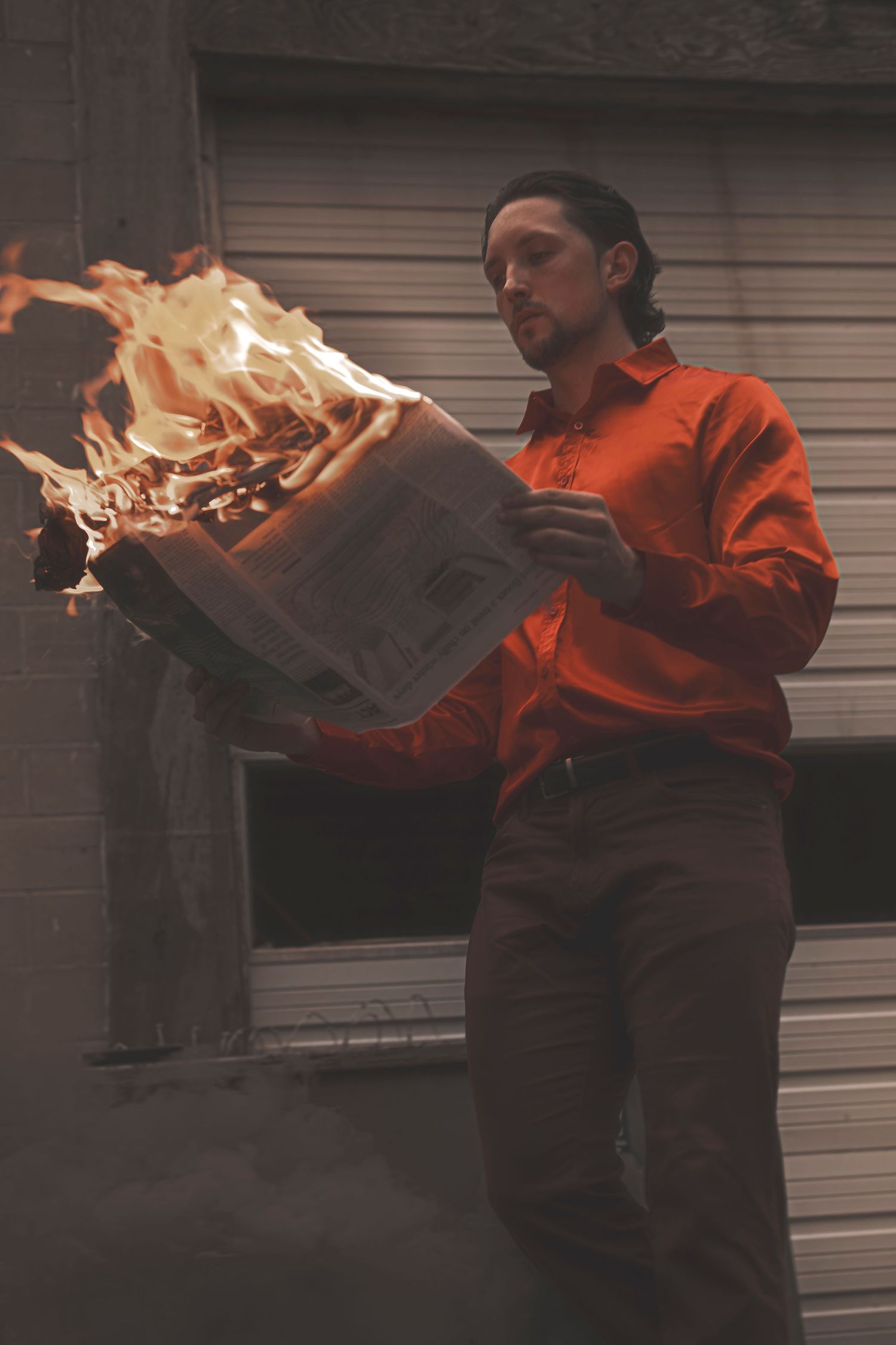 A person in an orange jacket holds a flaming laptop computer creating dramatic lighting effect.
