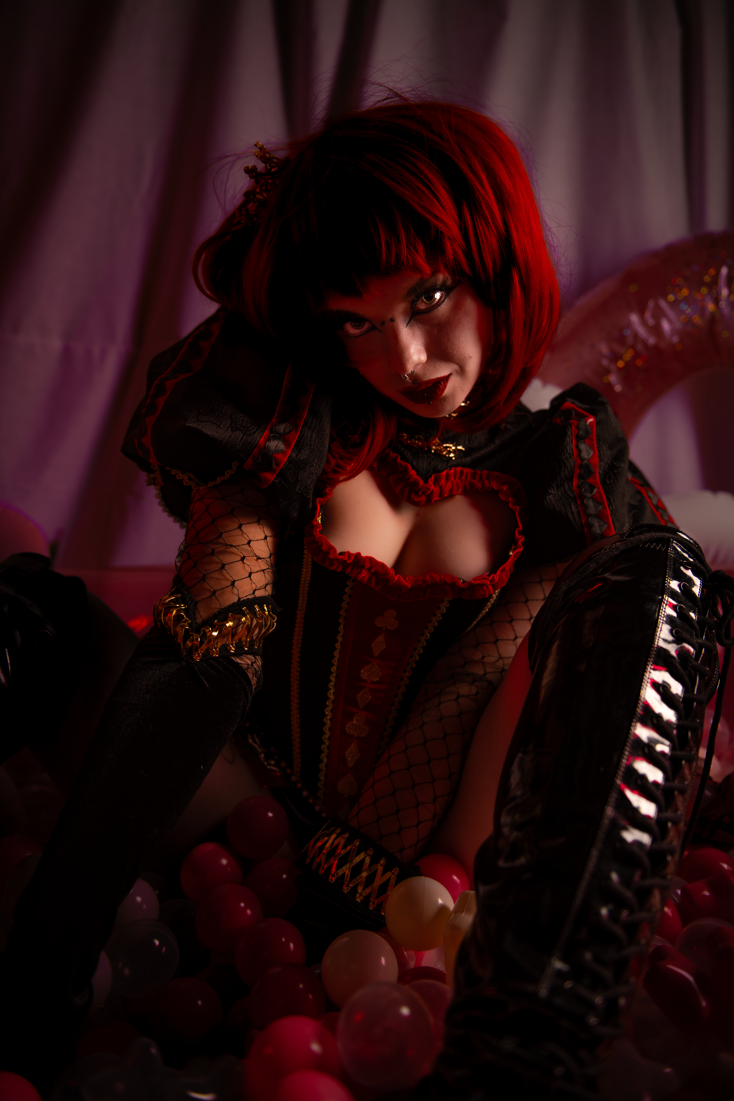 A gothic themed photoshoot with red lighting features dark clothing, corsets and ornate details in a dramatic setting.