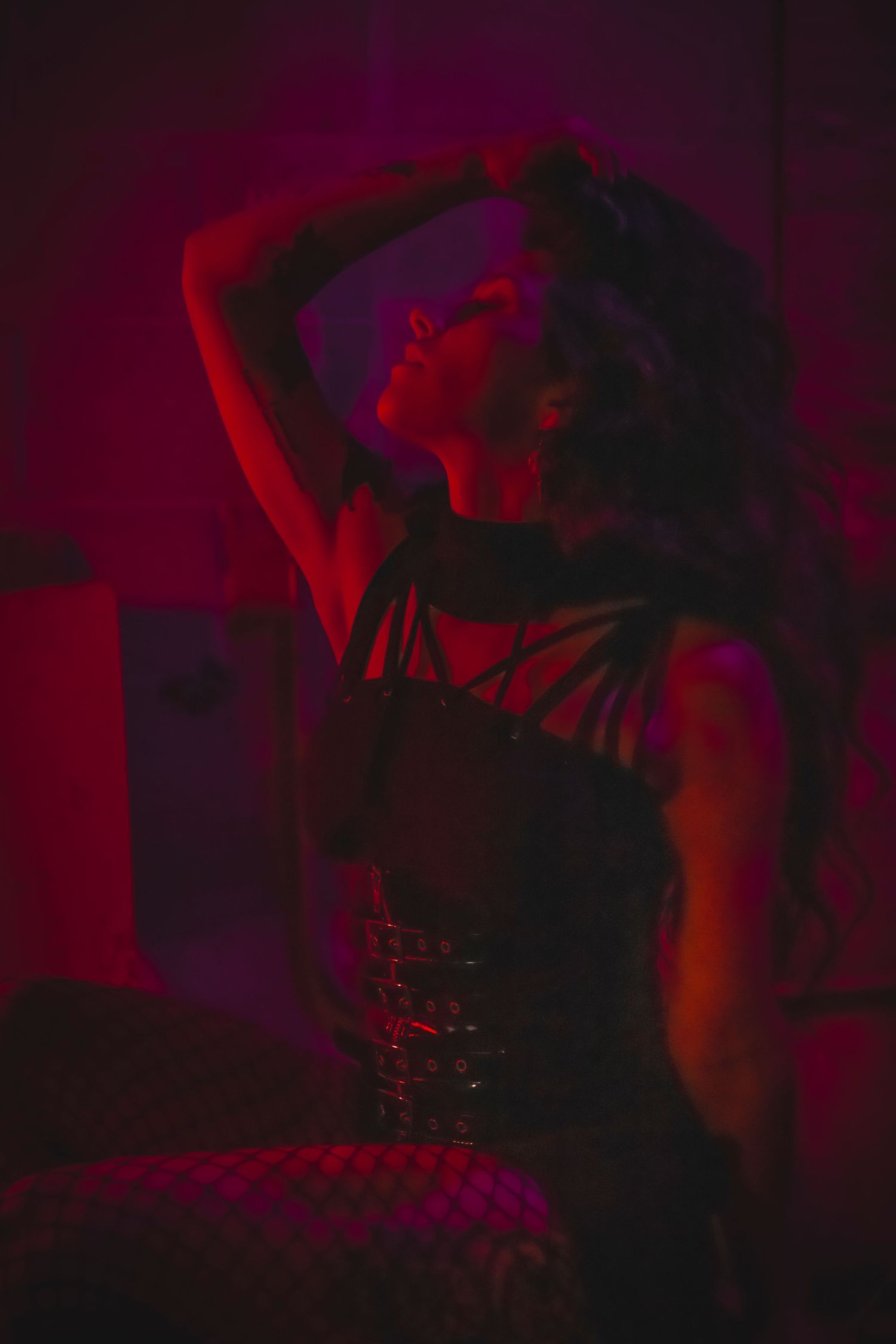 Silhouetted DJ performs with electronic music equipment against dramatic red lighting on nightclub stage.