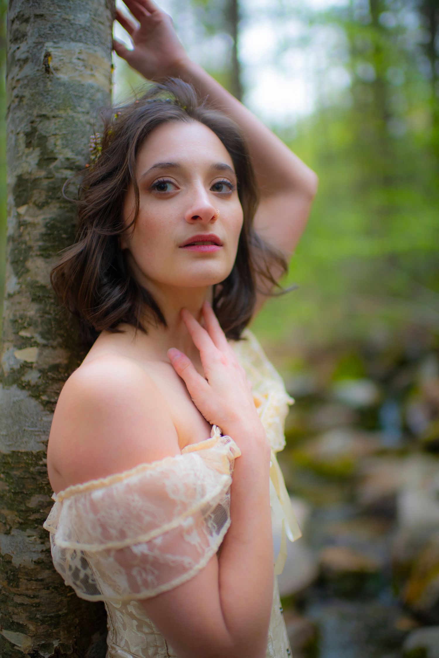 Artistic portrait in a forest setting with soft lighting and delicate lace details.