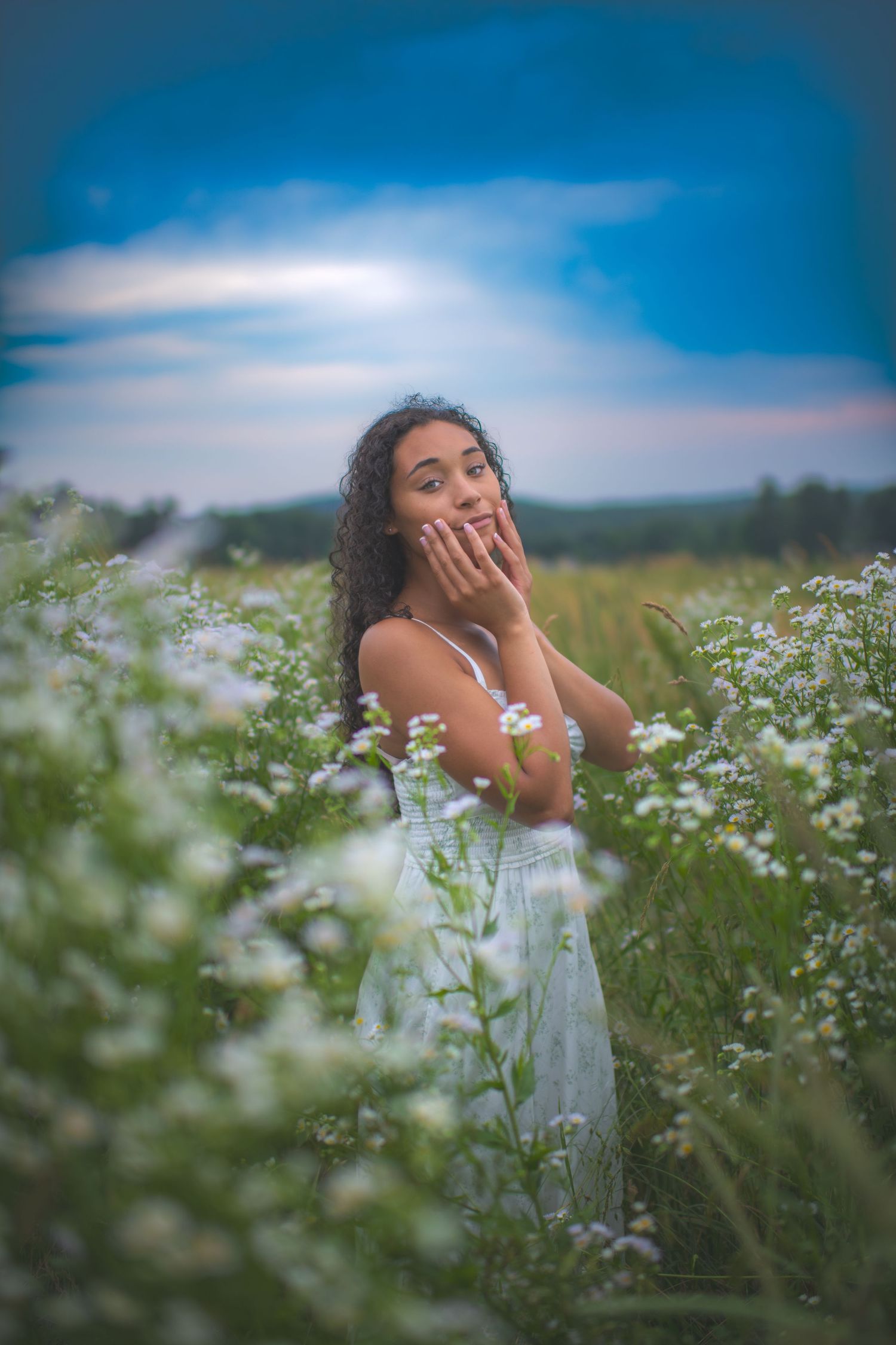 Woman in white dress poses playfully among blooming white wildflowers.