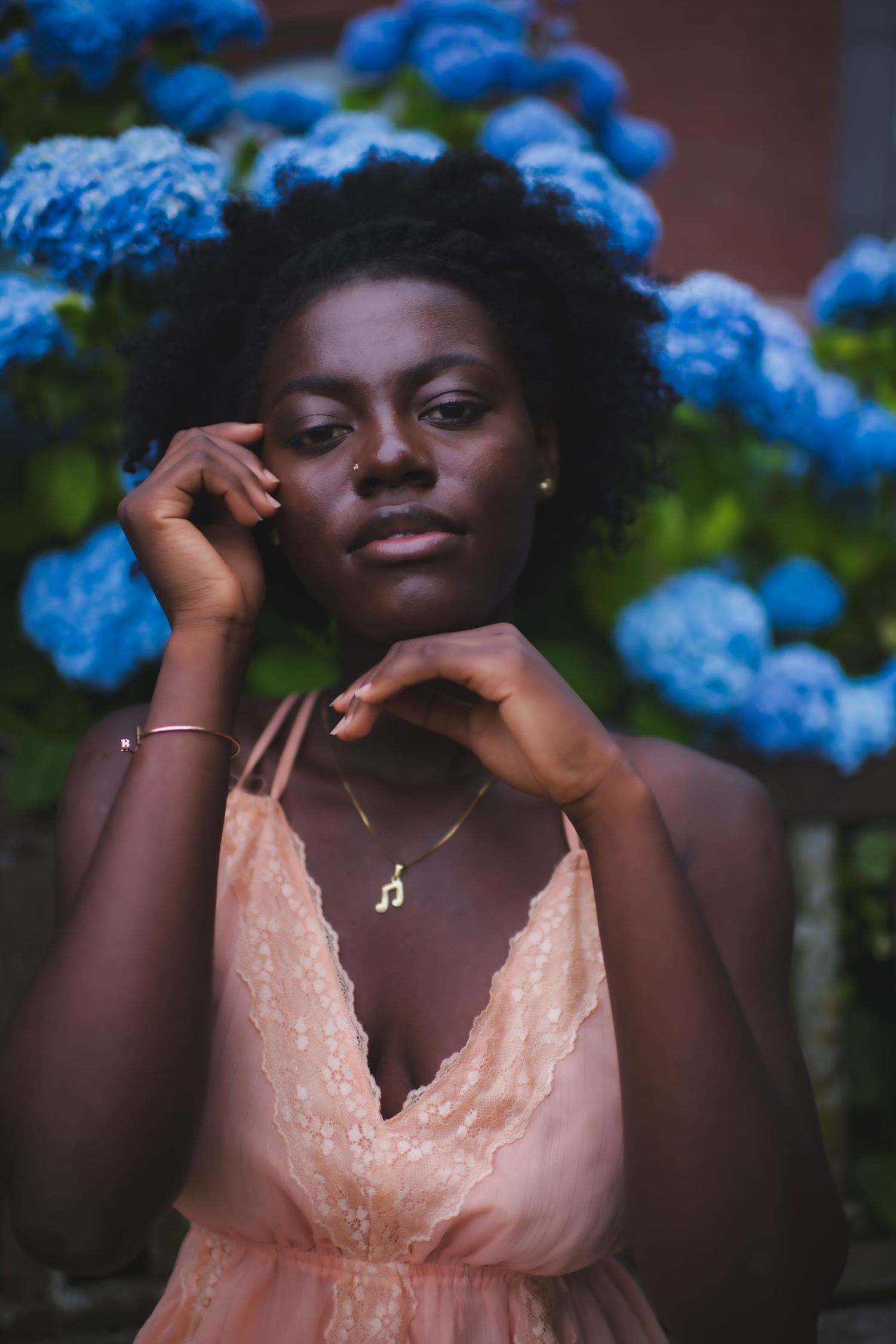 A gentle fashion portrait with delicate jewelry against a backdrop of blue flowers.