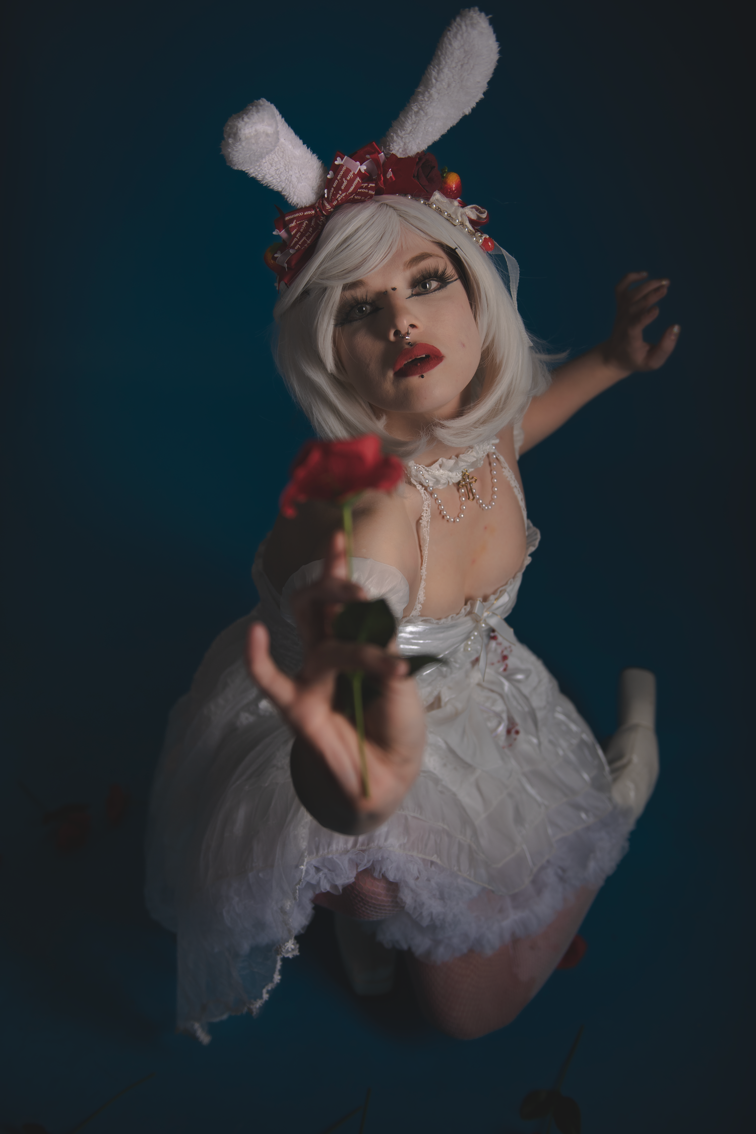 Dramatic photo of figure in white tulle dress with bunny ears against dark background.