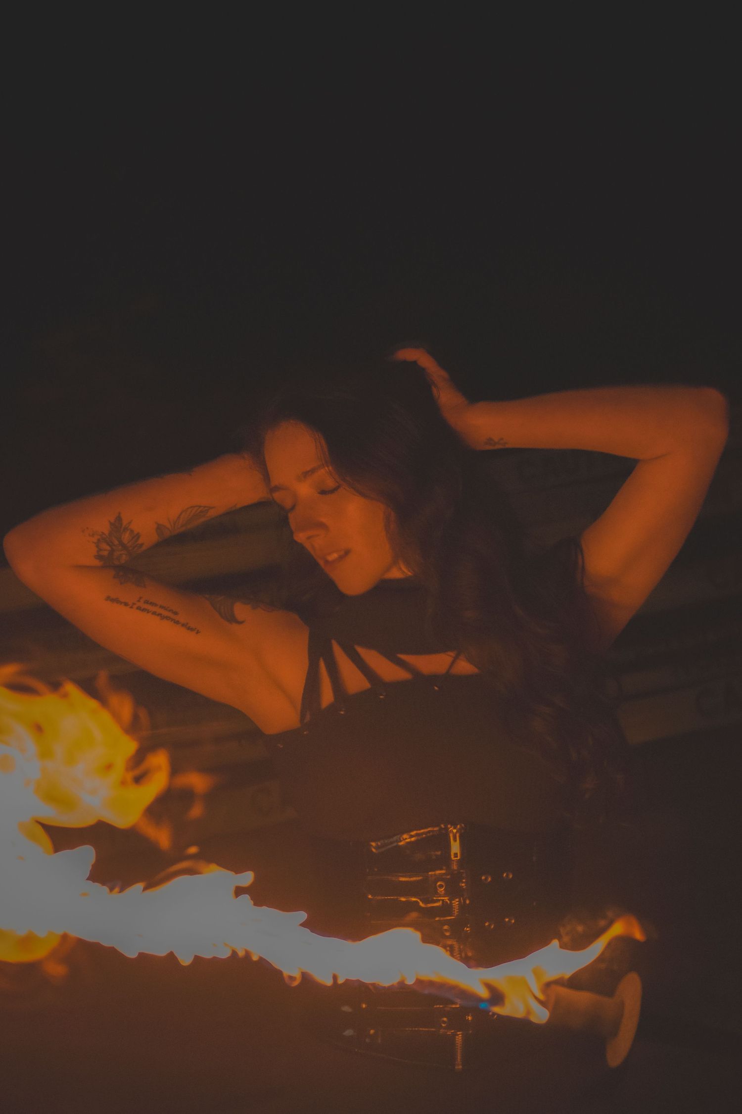 A person poses dramatically in the dark with fire illuminating the scene in warm orange tones.