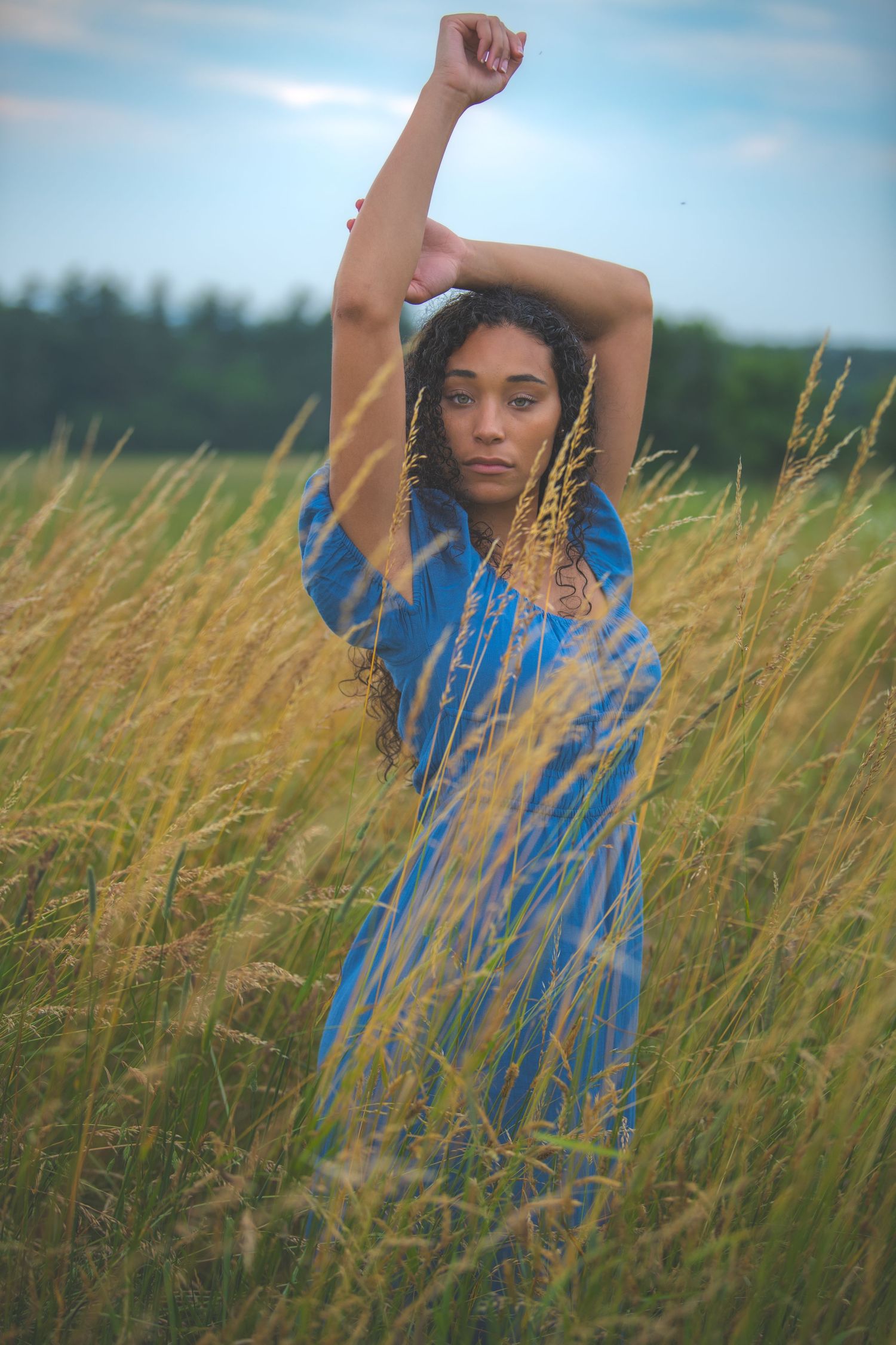 Woman in blue dress stretches gracefully among tall summer grass.