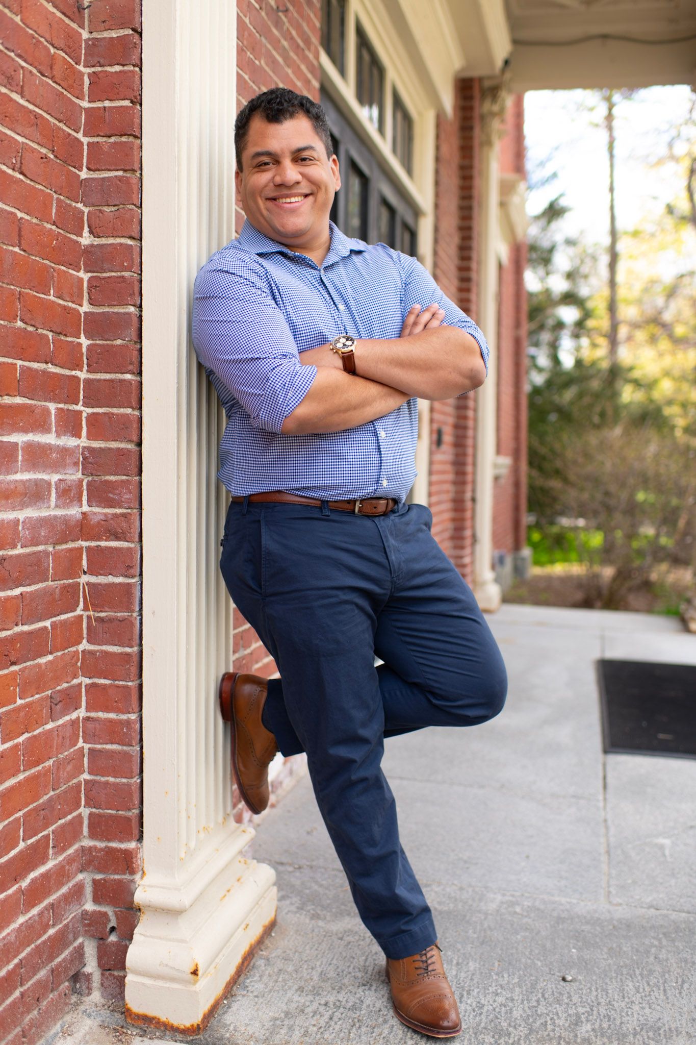 Professional pose against white column wearing blue striped shirt and navy pants.