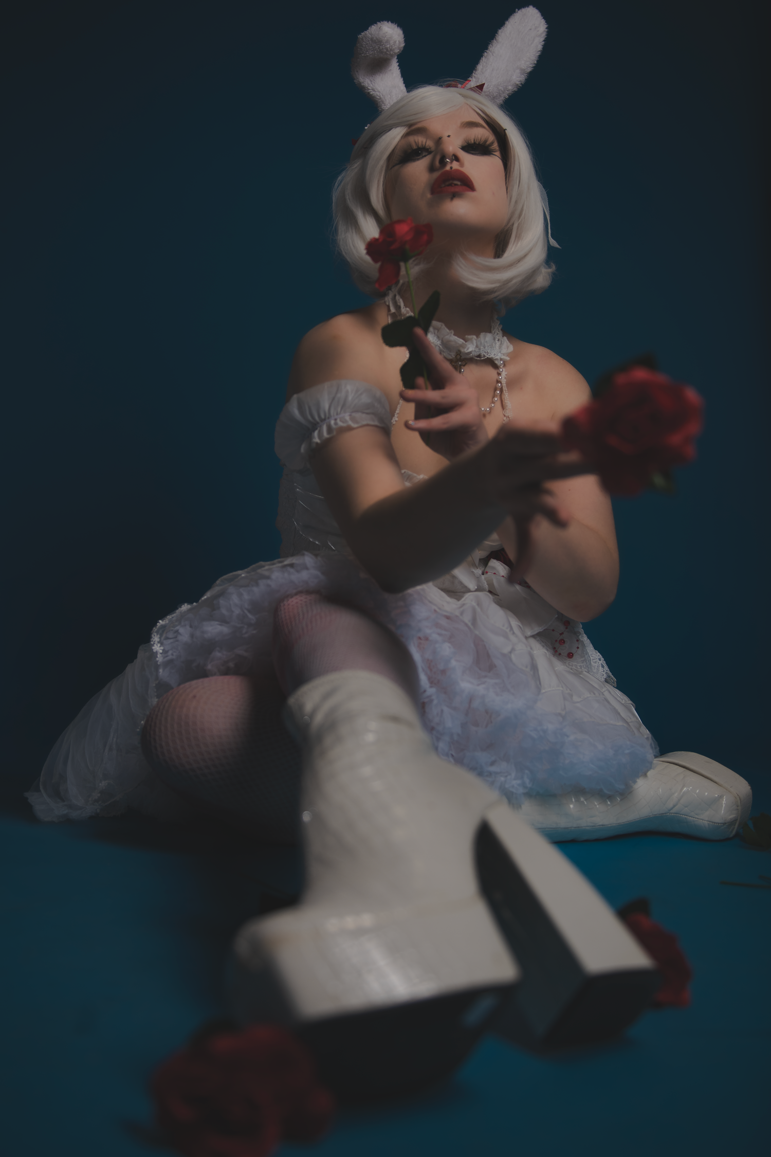 Artistic cosplay photography featuring a white dress, bunny ears, and red roses against a dark turquoise background.