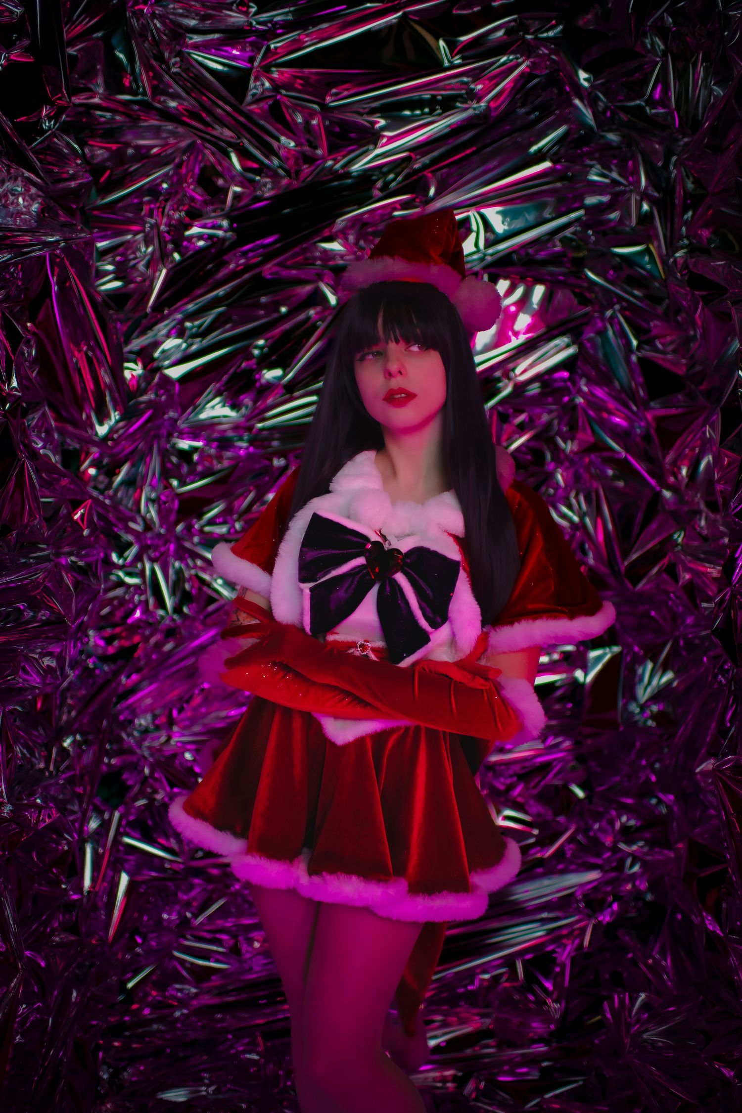 Figure in a red dress with black bow poses against metallic purple backdrop in dramatic lighting.