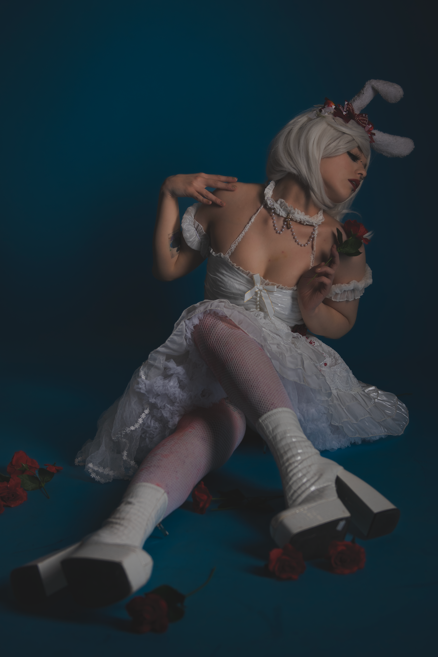Theatrical pose of person in white dress and bunny ears on dark background.
