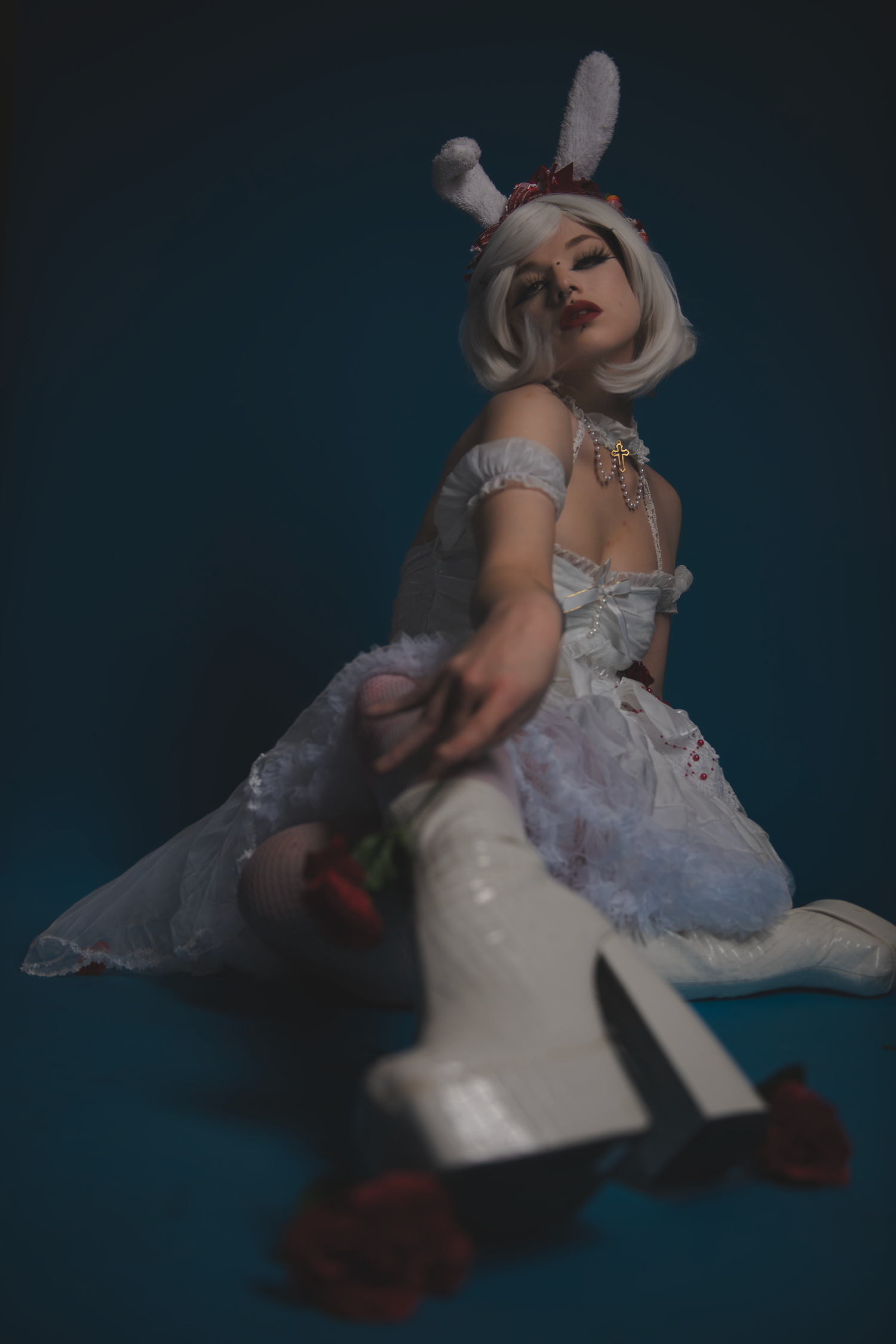 Figure in a white lacy dress and bunny ears poses dramatically against a dark background in moody lighting.