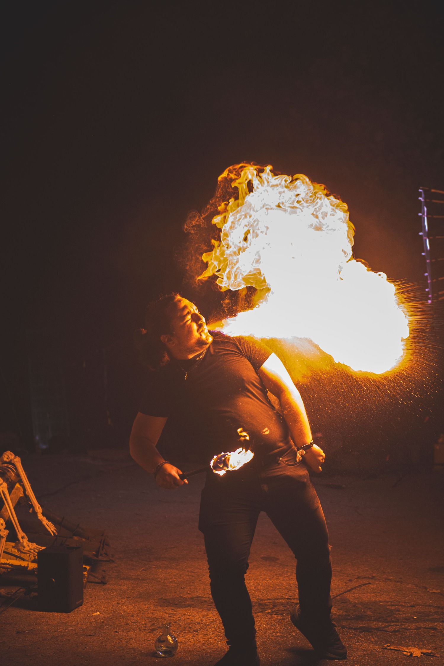 Fire breathing performer creating a large explosive flame burst in the darkness.