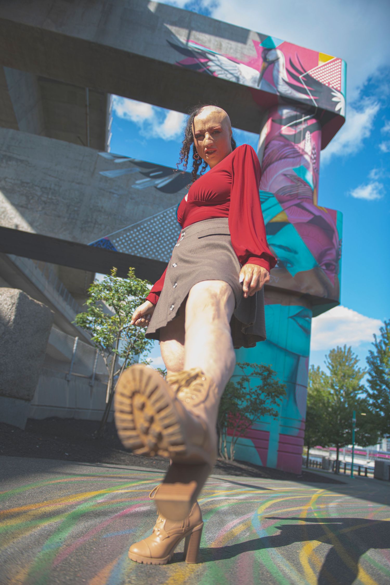 Low angle shot of someone wearing combat boots, a gray skirt and red sweater against a colorful mural background.
