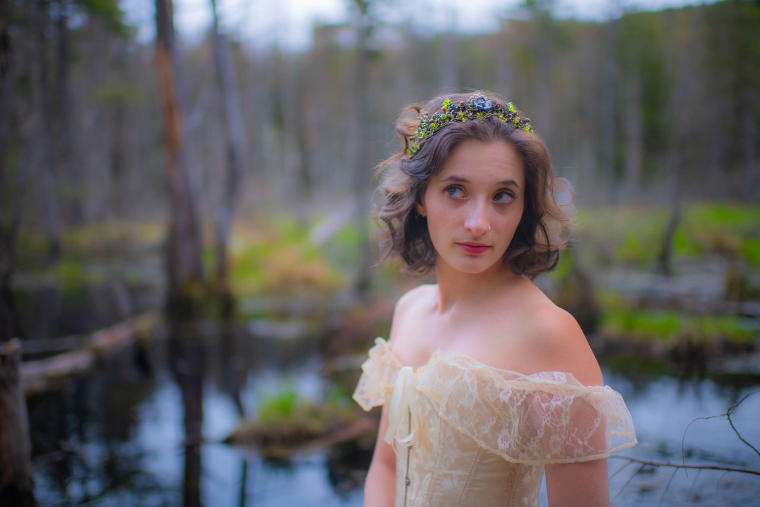 Person in vintage dress and floral crown poses by misty forest pond.