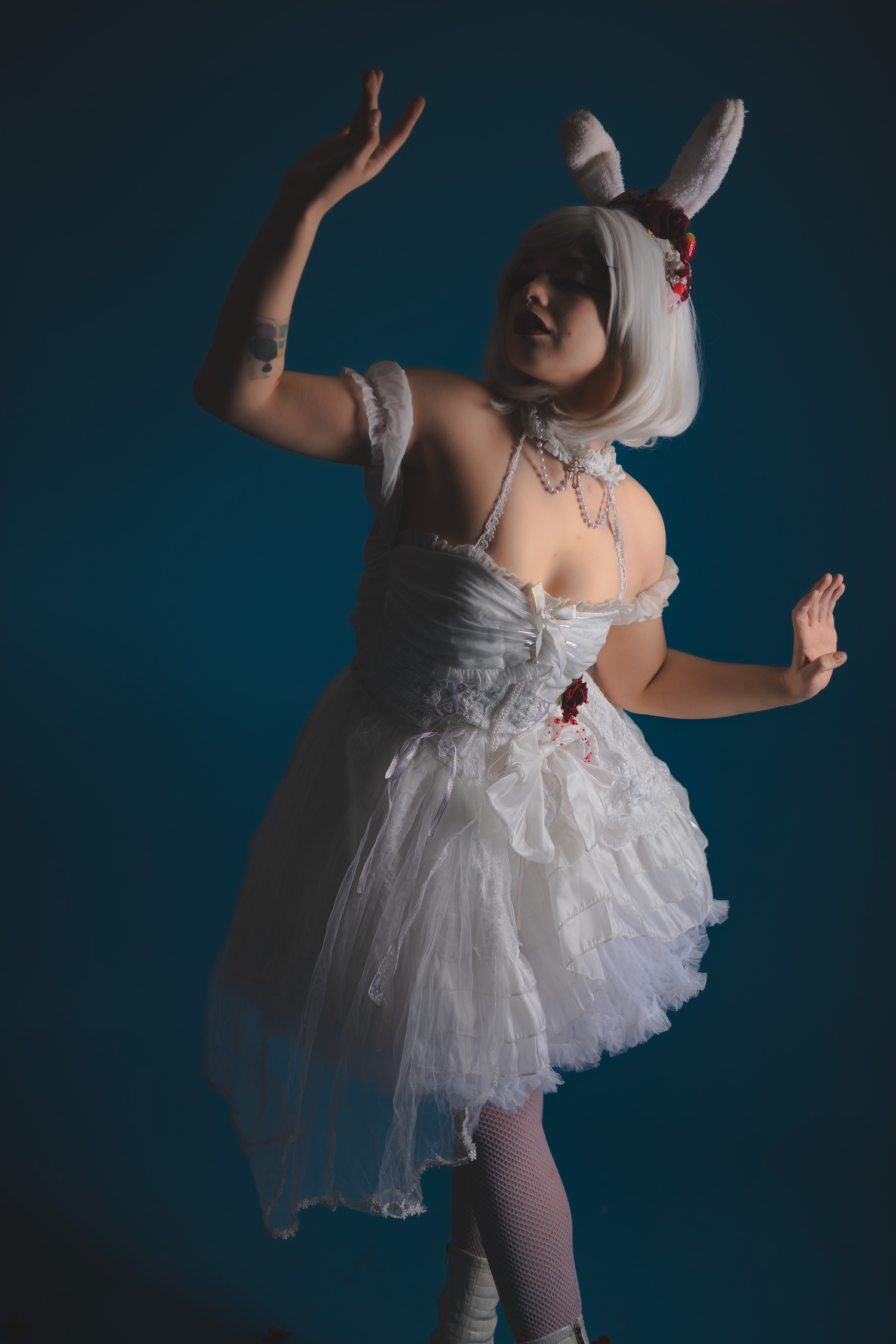 Artistic photoshoot featuring white dress and dramatic poses against deep blue backdrop.
