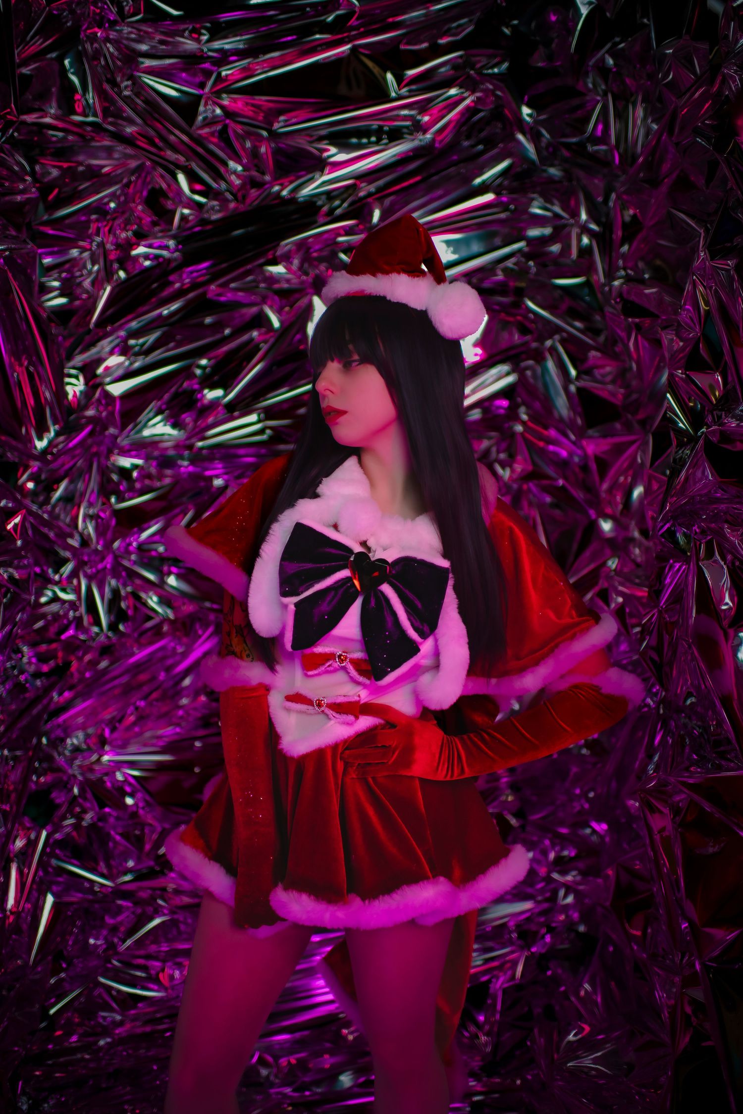 Person wearing festive red outfit and bow poses against shimmering metallic purple background.