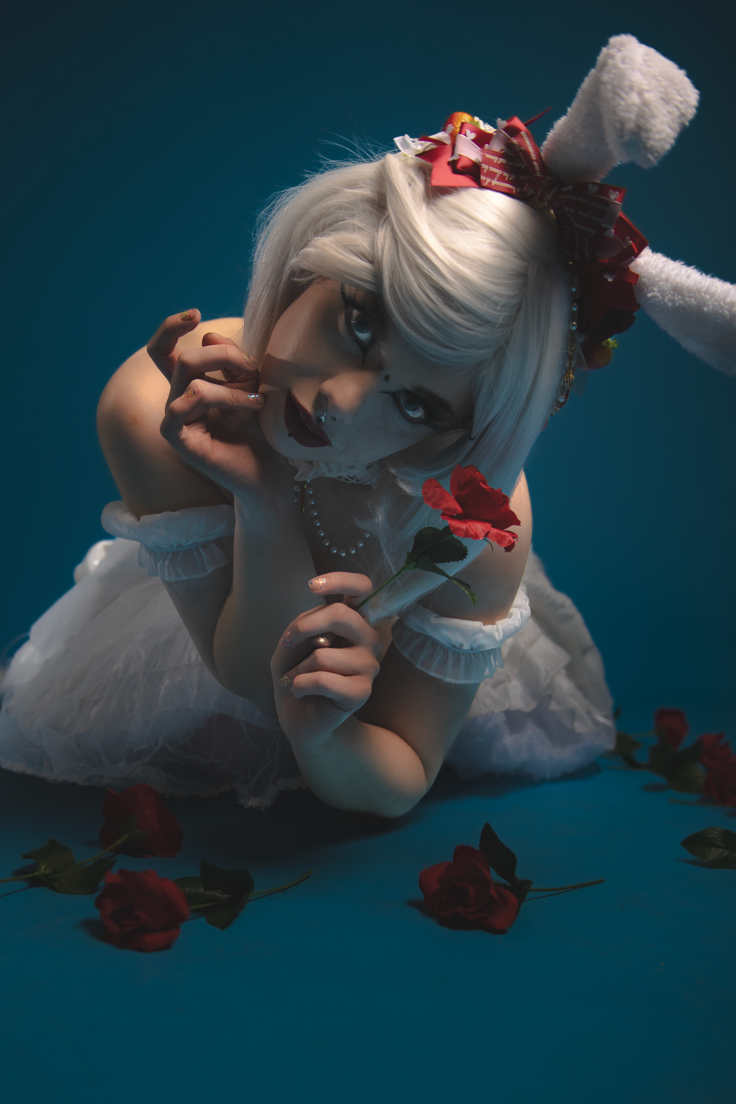 Artistic cosplay photo with white hair, red roses and ballet shoes against dark teal background.
