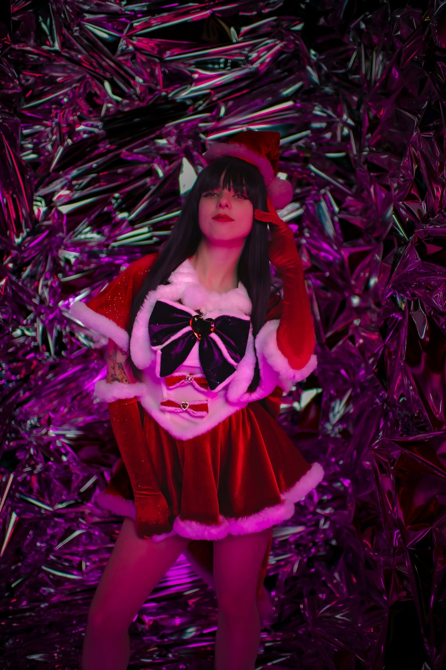A festive holiday photo with shimmering purple metallic background and red Santa costume in moody lighting.