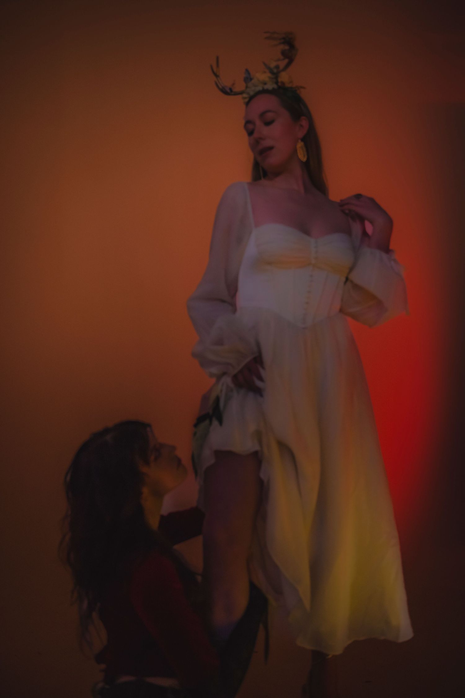Artistic portrait scene featuring performers in white dress with dramatic red and orange lighting effects.