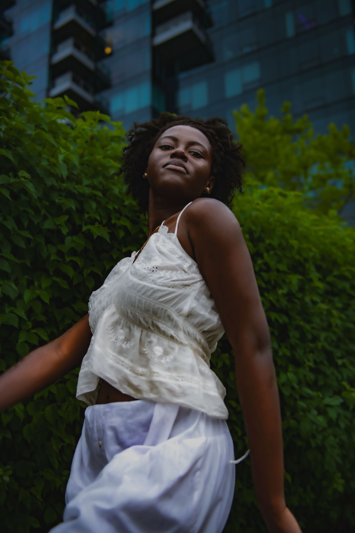 Artistic outdoor portrait with natural lighting against urban greenery and buildings.