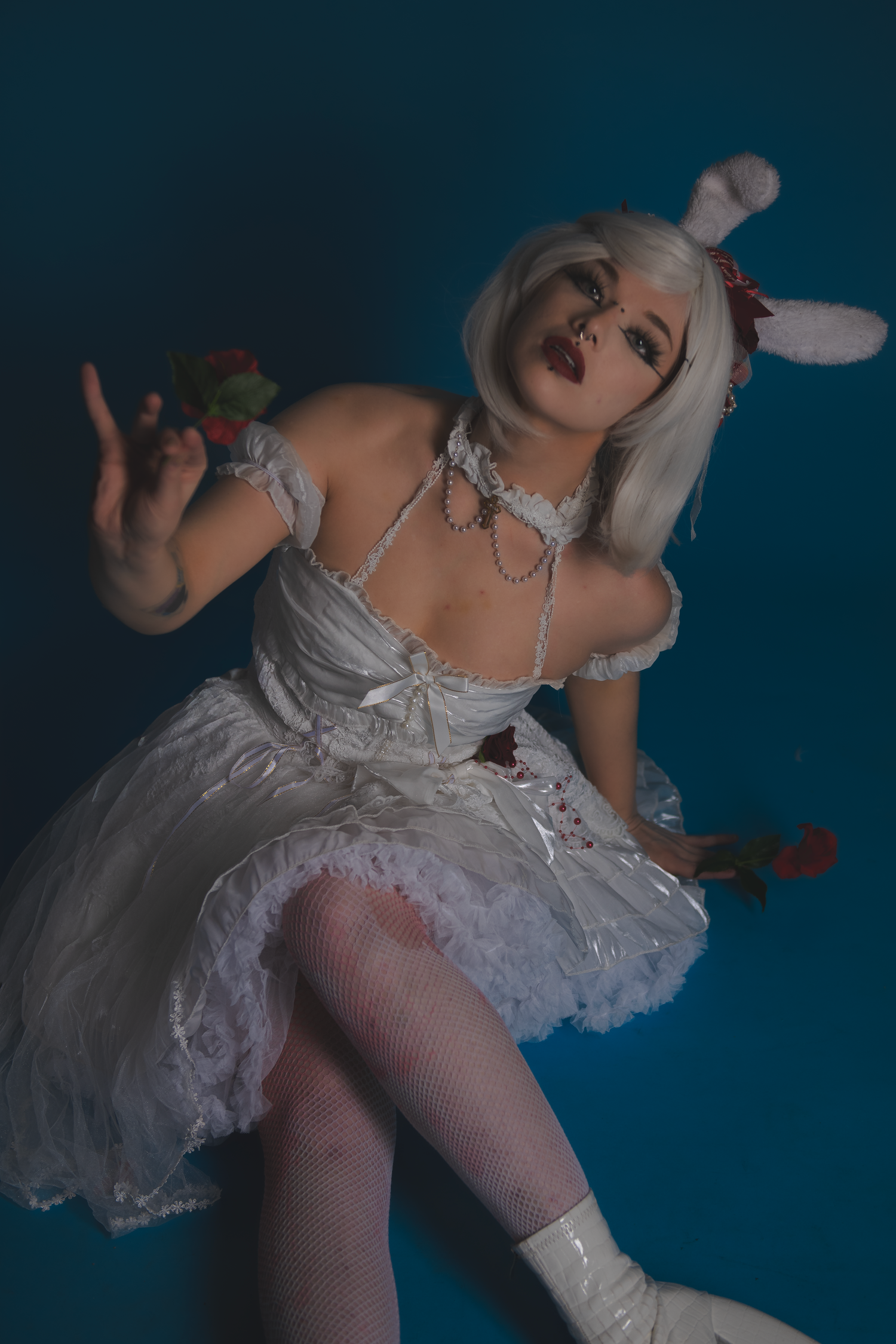 Whimsical fashion portrait with white costume, bunny ears and scattered rose petals in moody lighting.