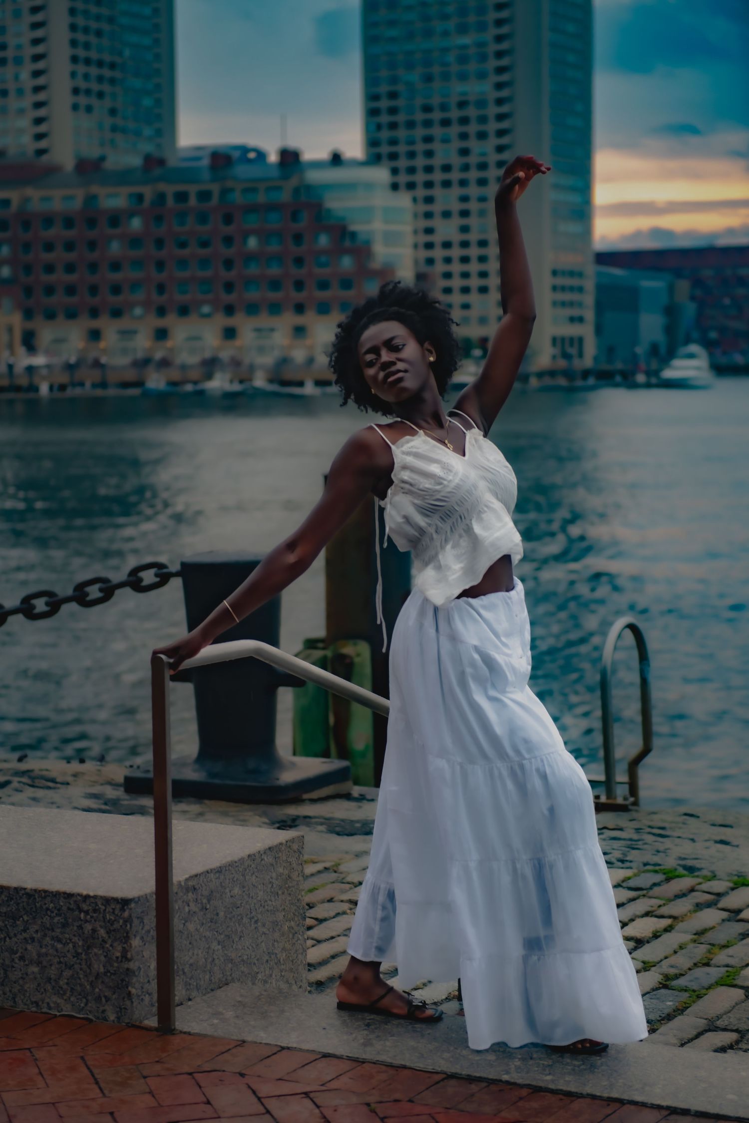 White flowing dress against waterfront cityscape at sunset.