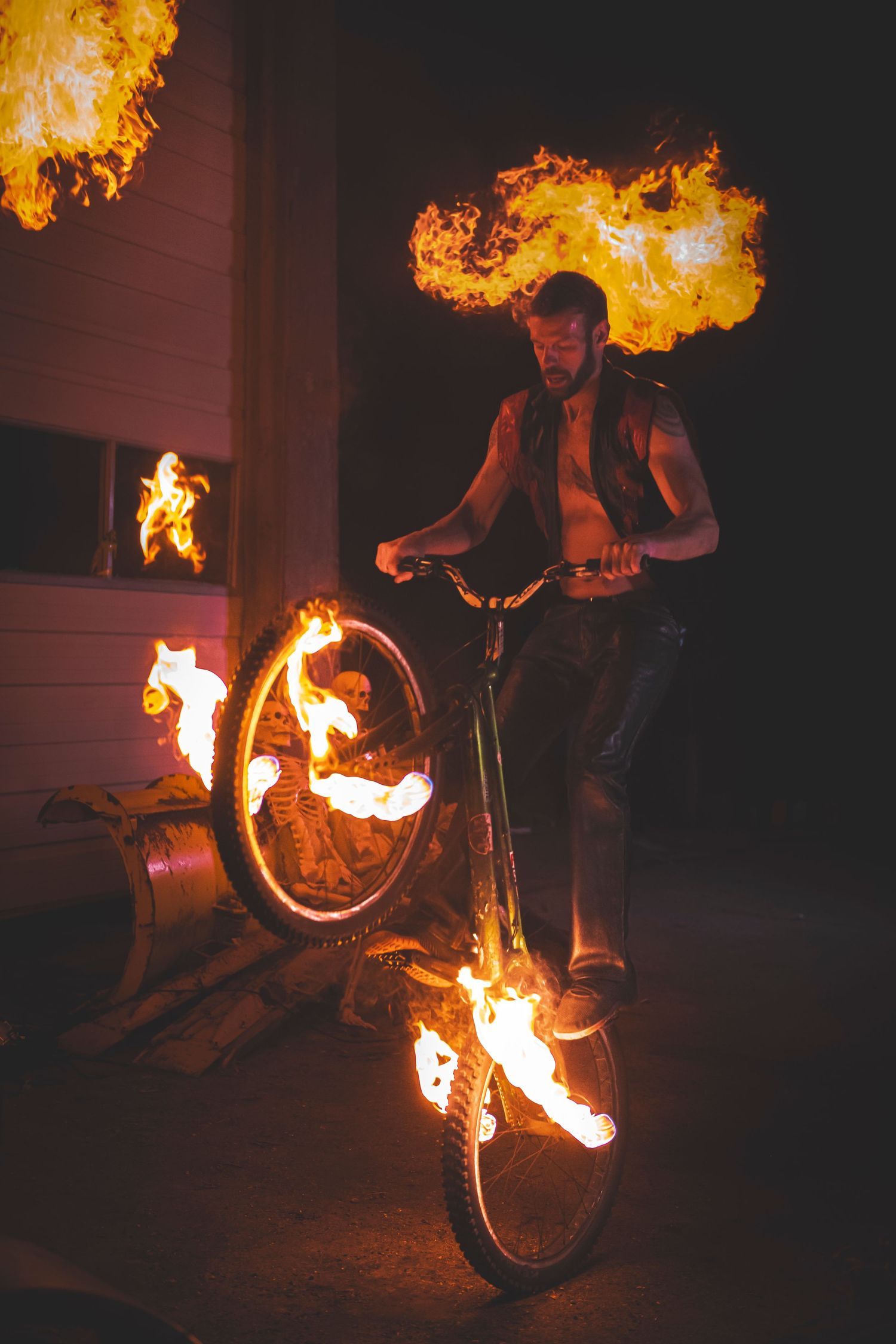 BMX rider performs stunts on a bicycle with flaming wheels while breathing fire at night.