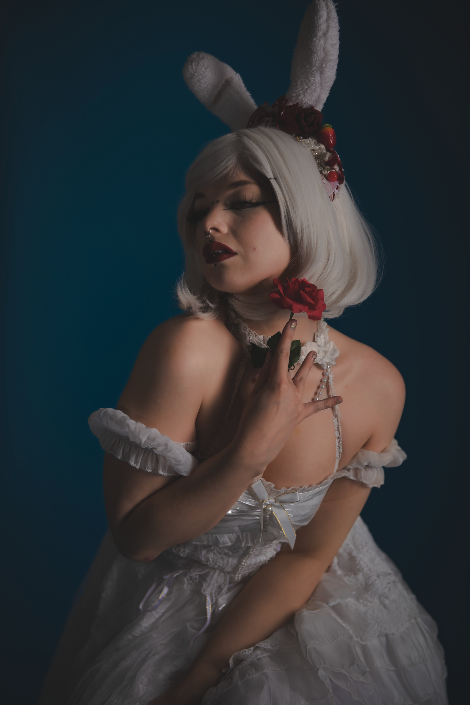 Dramatic boudoir photo of figure in white dress and bunny ears against dark background.