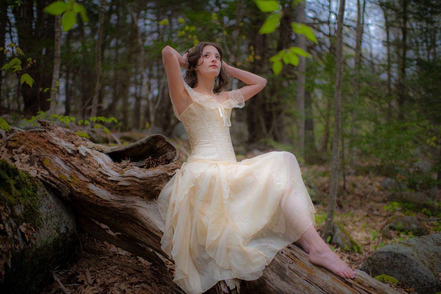 Ethereal figure in a cream dress reclines on a fallen log in a dreamy forest setting.