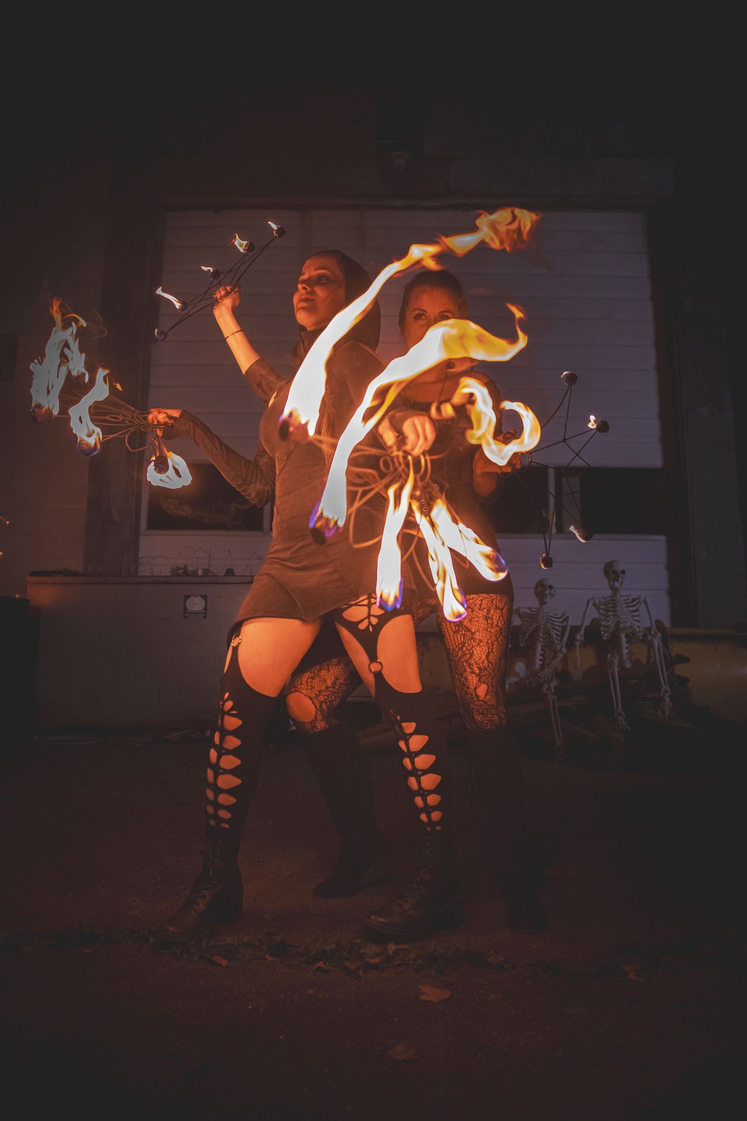 Fire performers swing blazing staffs in dramatic arcs against a dark background during a fire dance display.