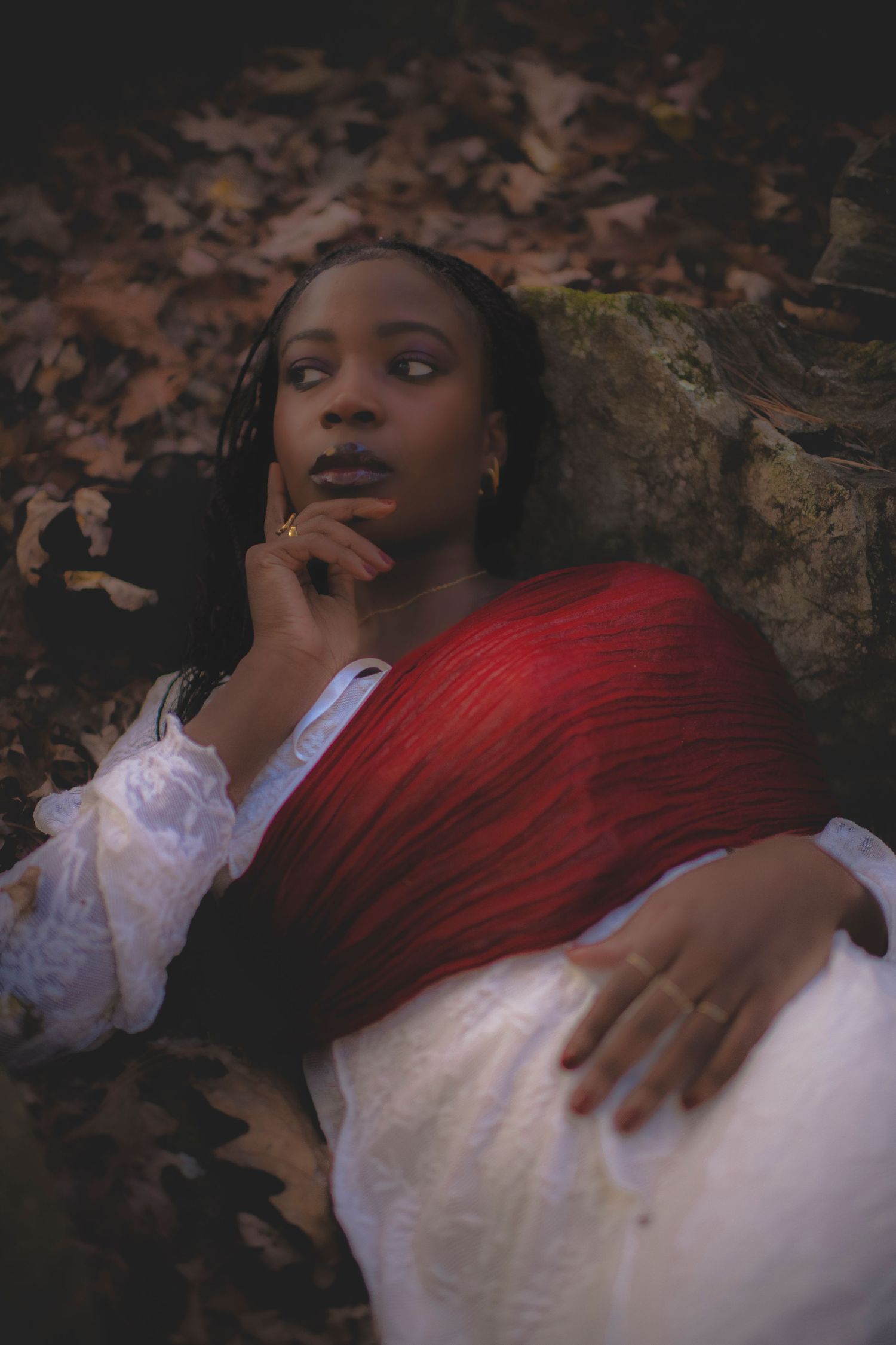Romantic portrait with white dress and red shawl against autumn forest floor.