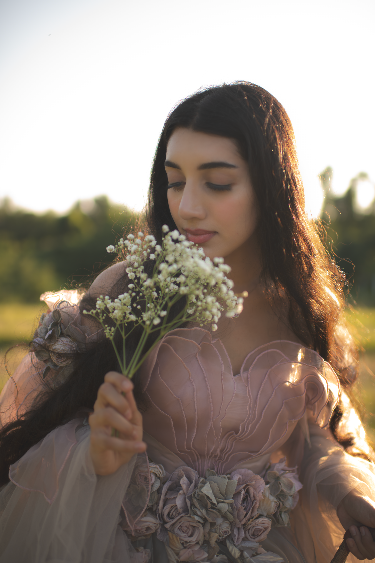 A dreamy portrait series of someone in a mauve dress holding wildflowers against golden sunlight in a field.