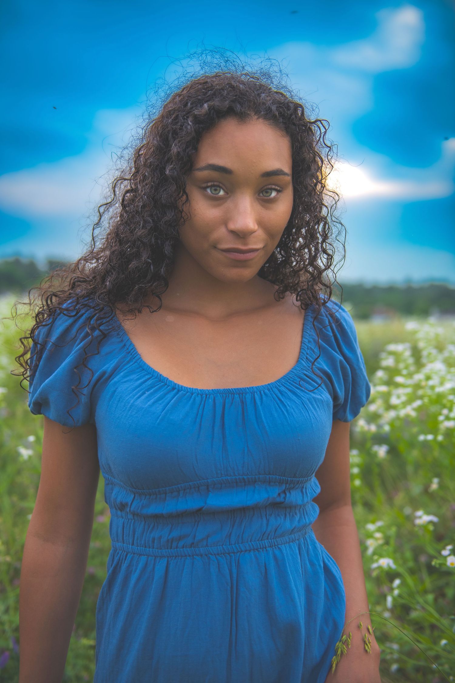 Woman in blue dress poses in a field of wildflowers against a bright blue sky.