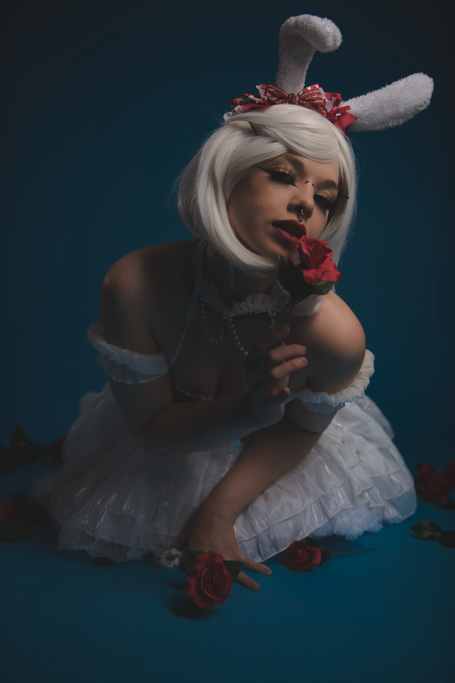 A figure in white dress and red lipstick poses dramatically in a dark studio setting, creating a series of ethereal images.