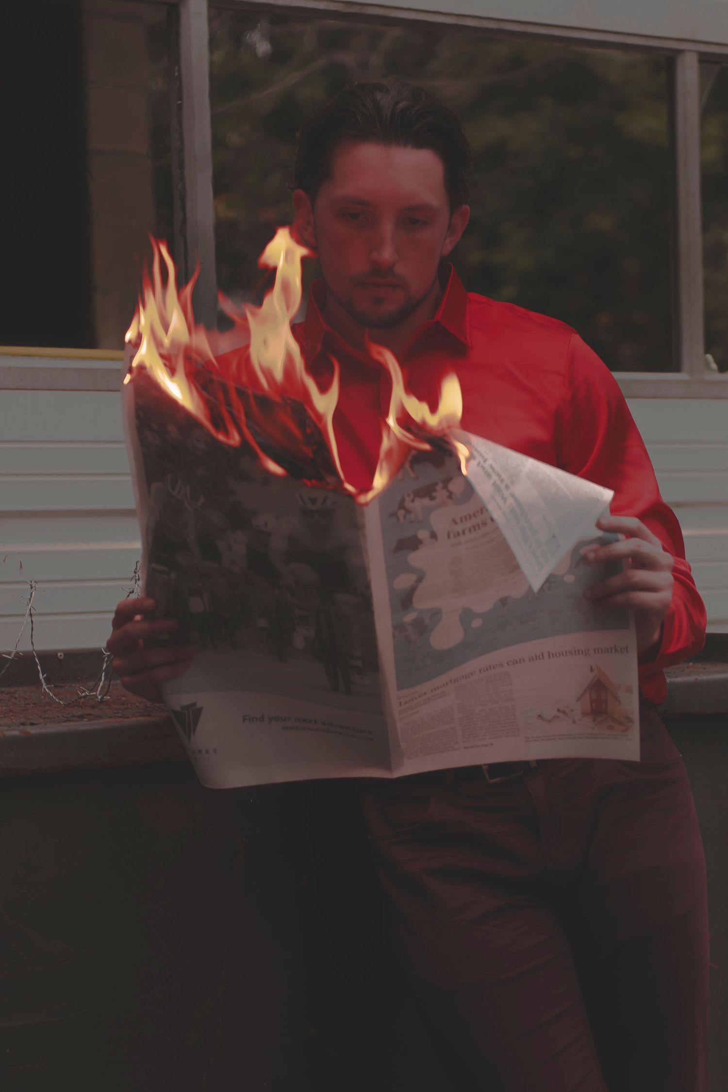A sequence showing a person reading a newspaper that becomes engulfed in flames while sitting indoors.