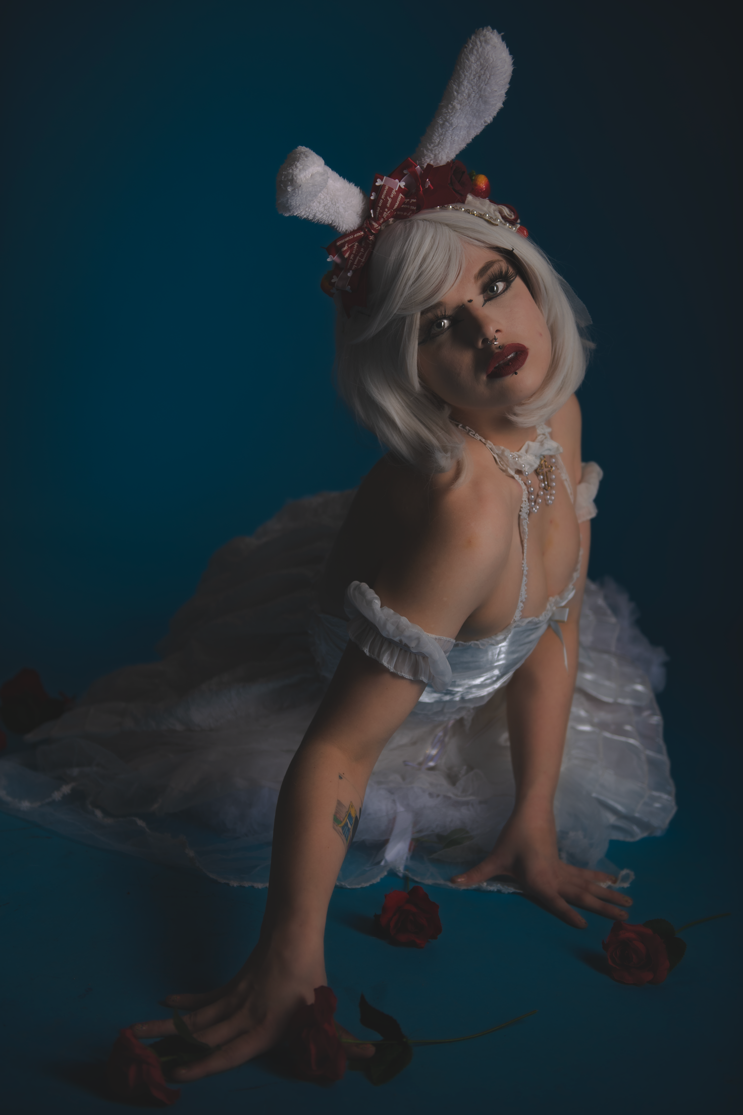 A model in white costume with bunny ears poses against dark background in dramatic lighting.