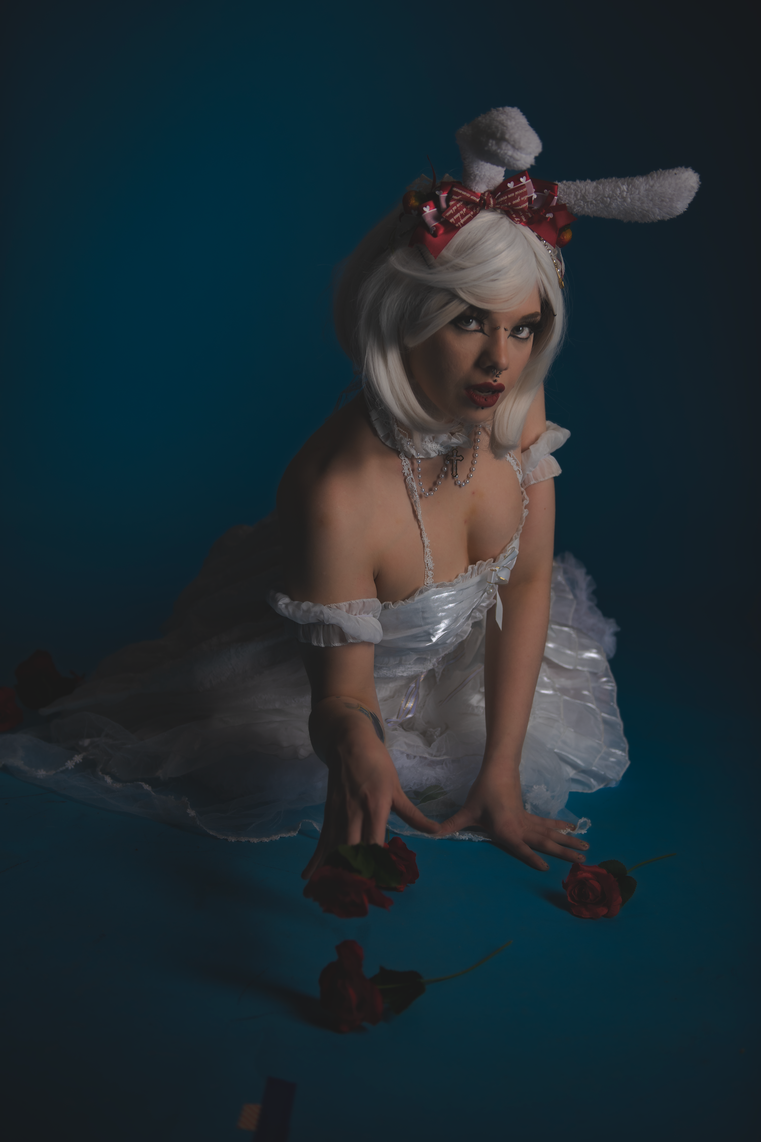 Figure in white dress crawling on dark floor with scattered roses.
