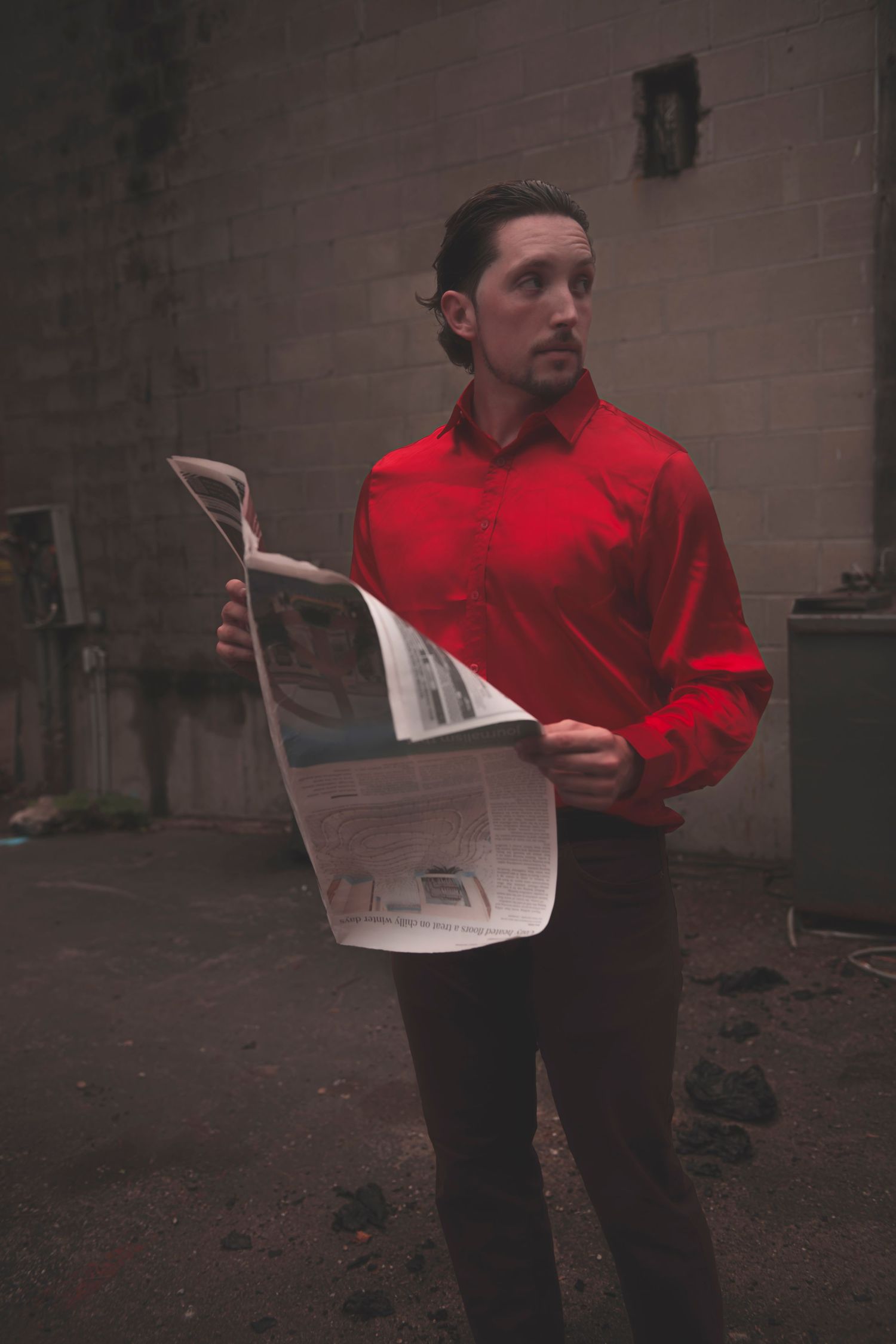 A person in a red shirt reads a section of newspaper outside against a dark background in a multi-panel sequence.