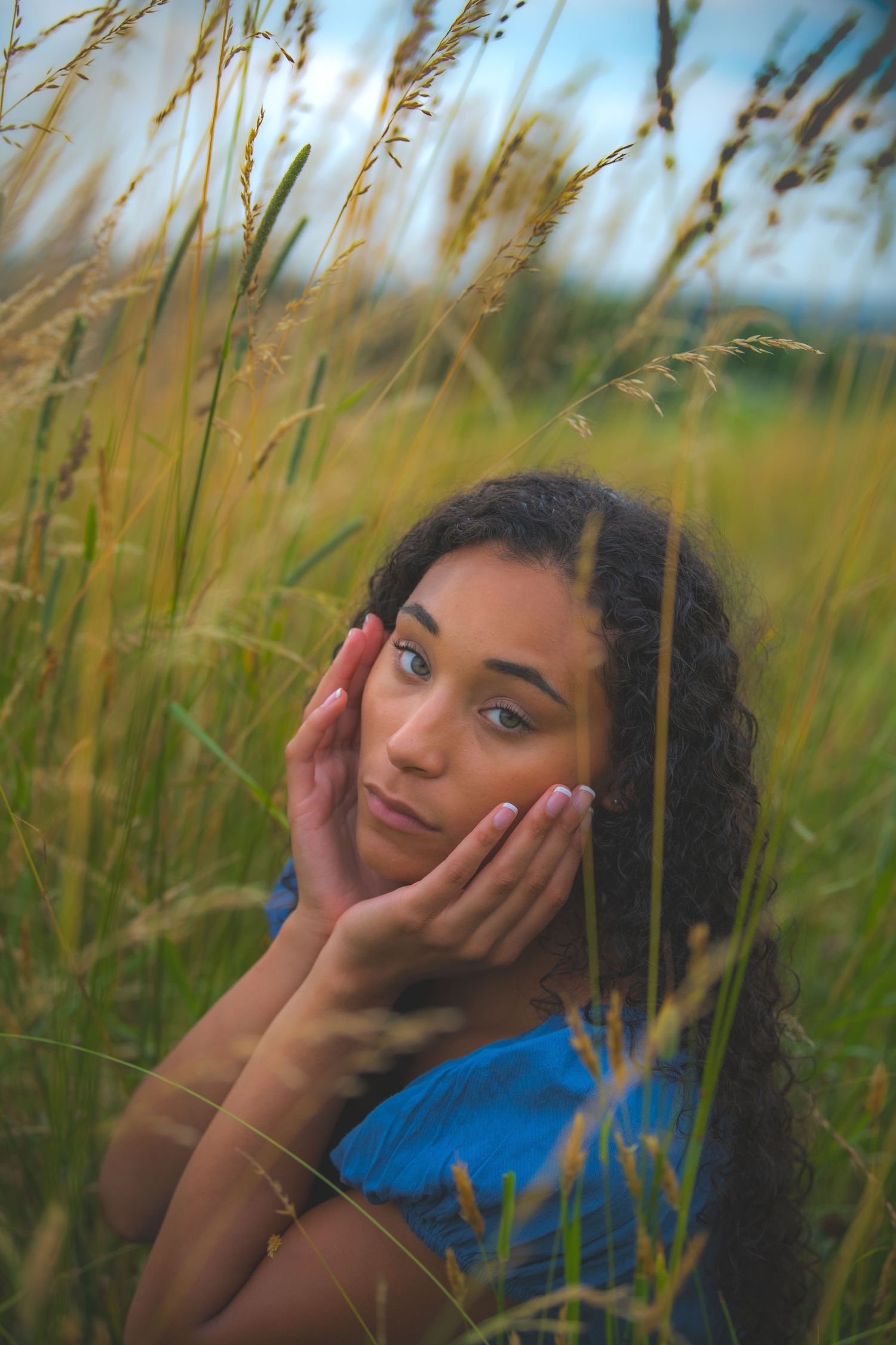 Artistic portrait through tall grass of a woman gently touching her face.