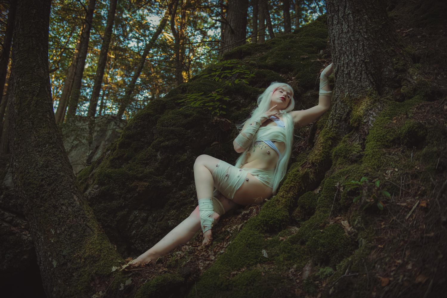 A figure in a flowy white dress poses gracefully in a moody forest setting creating an ethereal woodland scene.