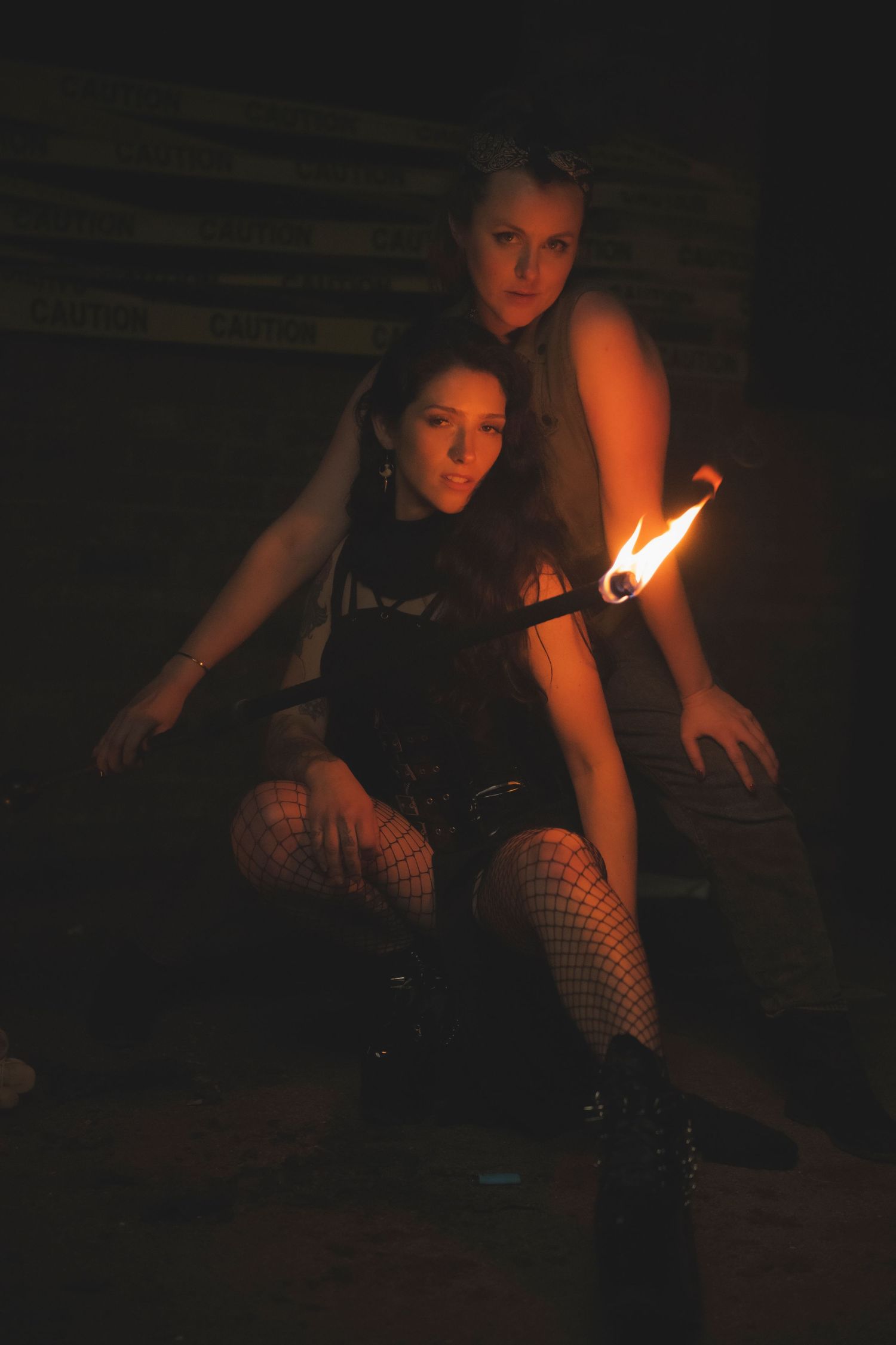 Two alternative-style performers posing dramatically in dark lighting with a small flame visible.