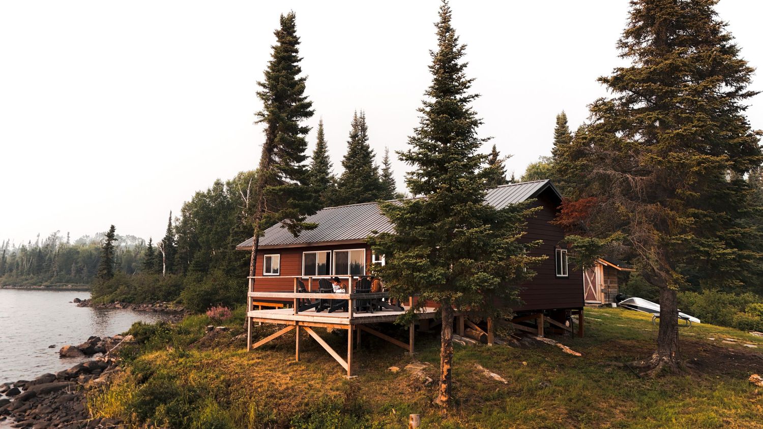 Panoramic view of evergreen trees and rustic cabins along a remote shoreline.