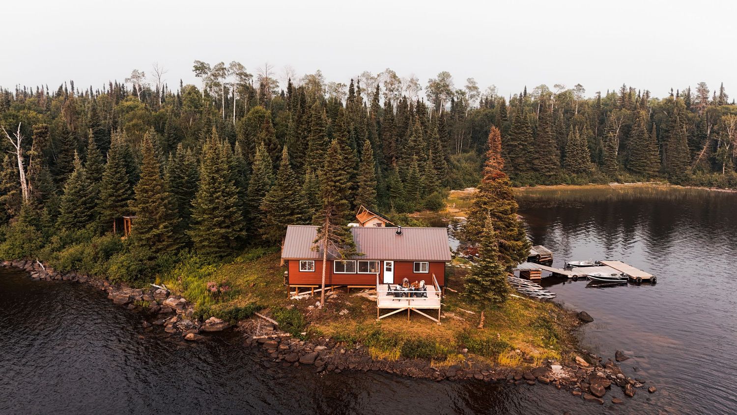Aerial panorama of waterfront cottages surrounded by dense pine forest.