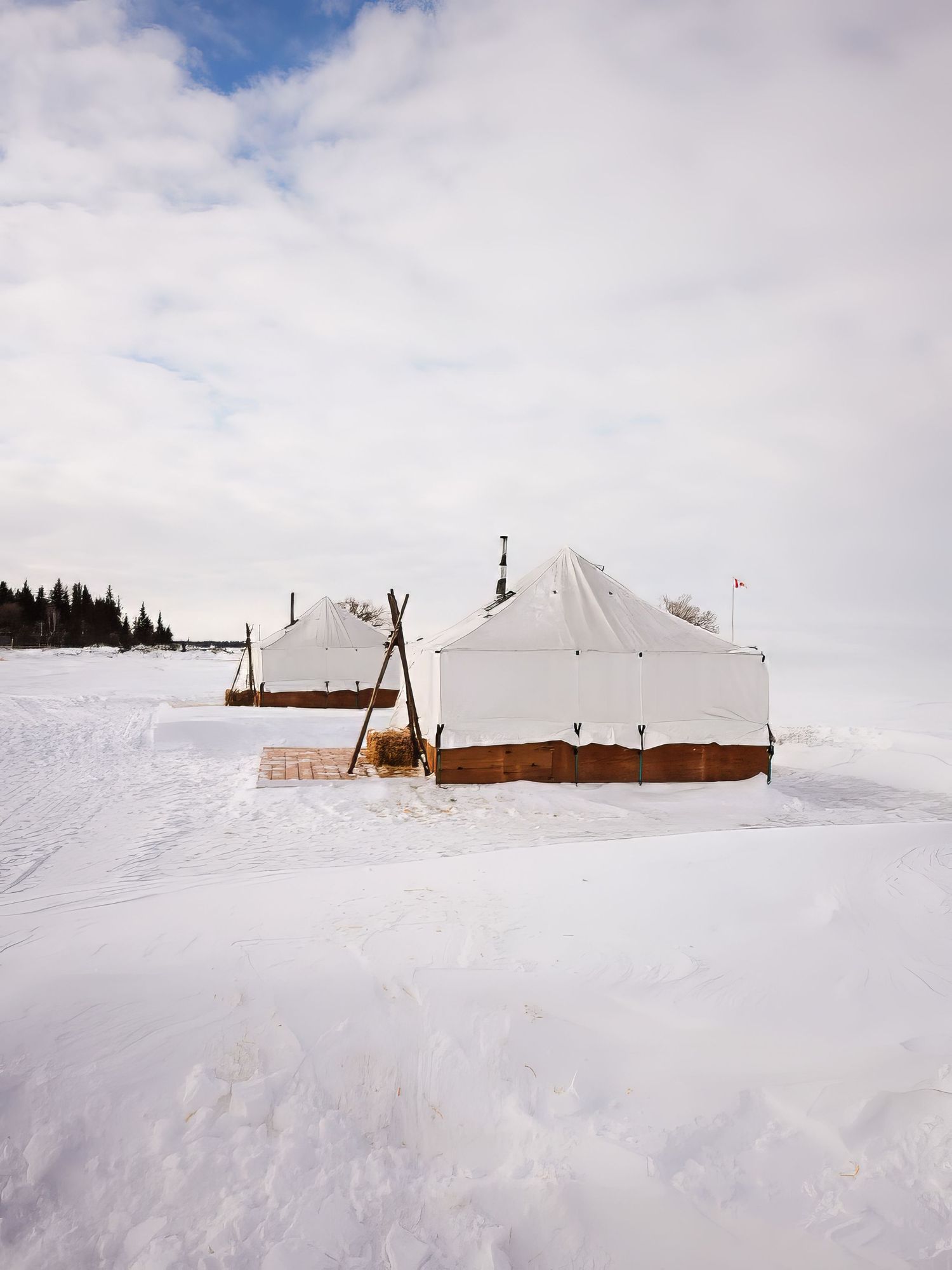 White snow-covered landscape with tents and structures against a cloudy winter sky.